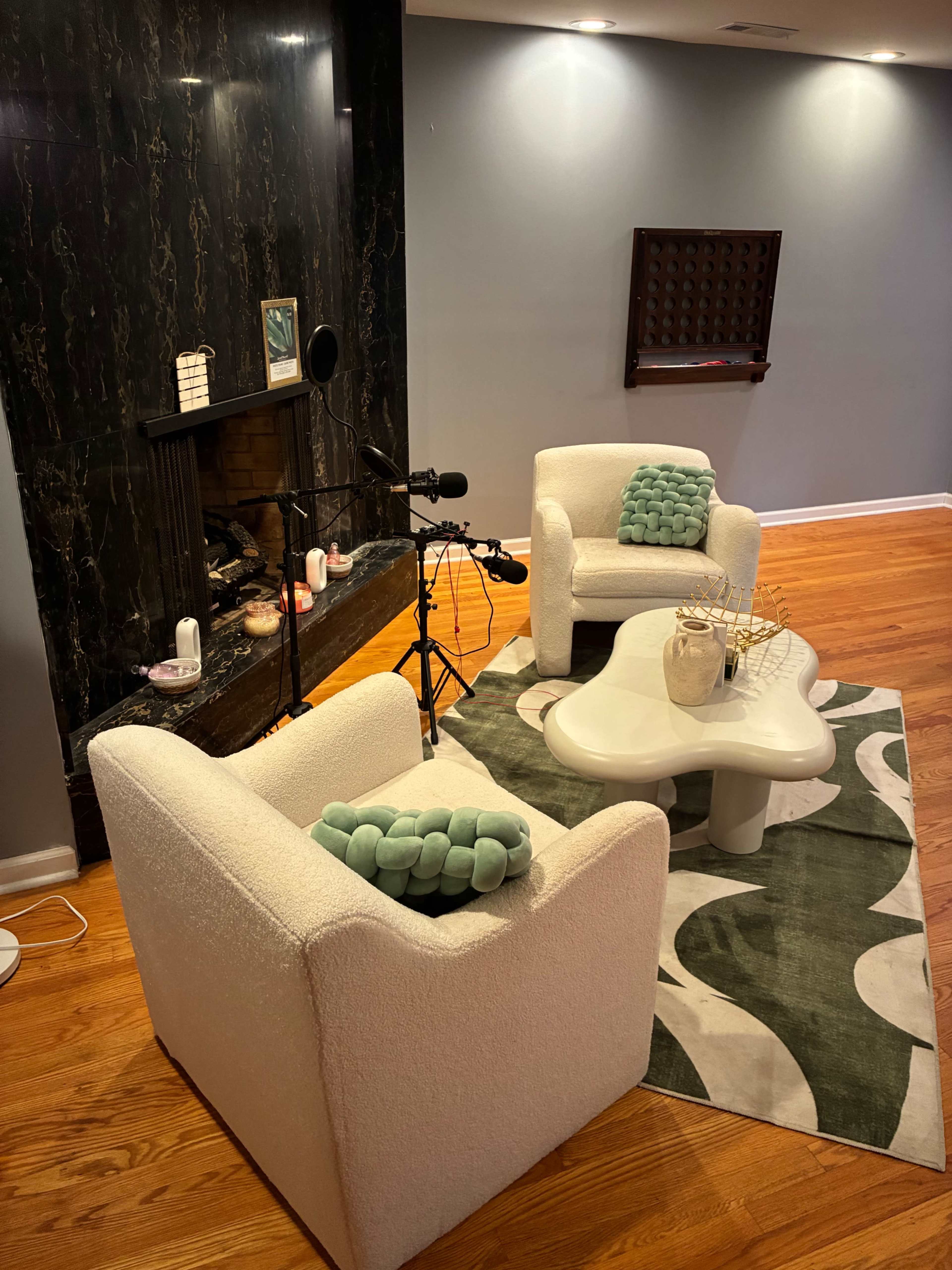 The image shows a cozy living room with two white chairs, a coffee table, a patterned rug, and a fireplace in the background.