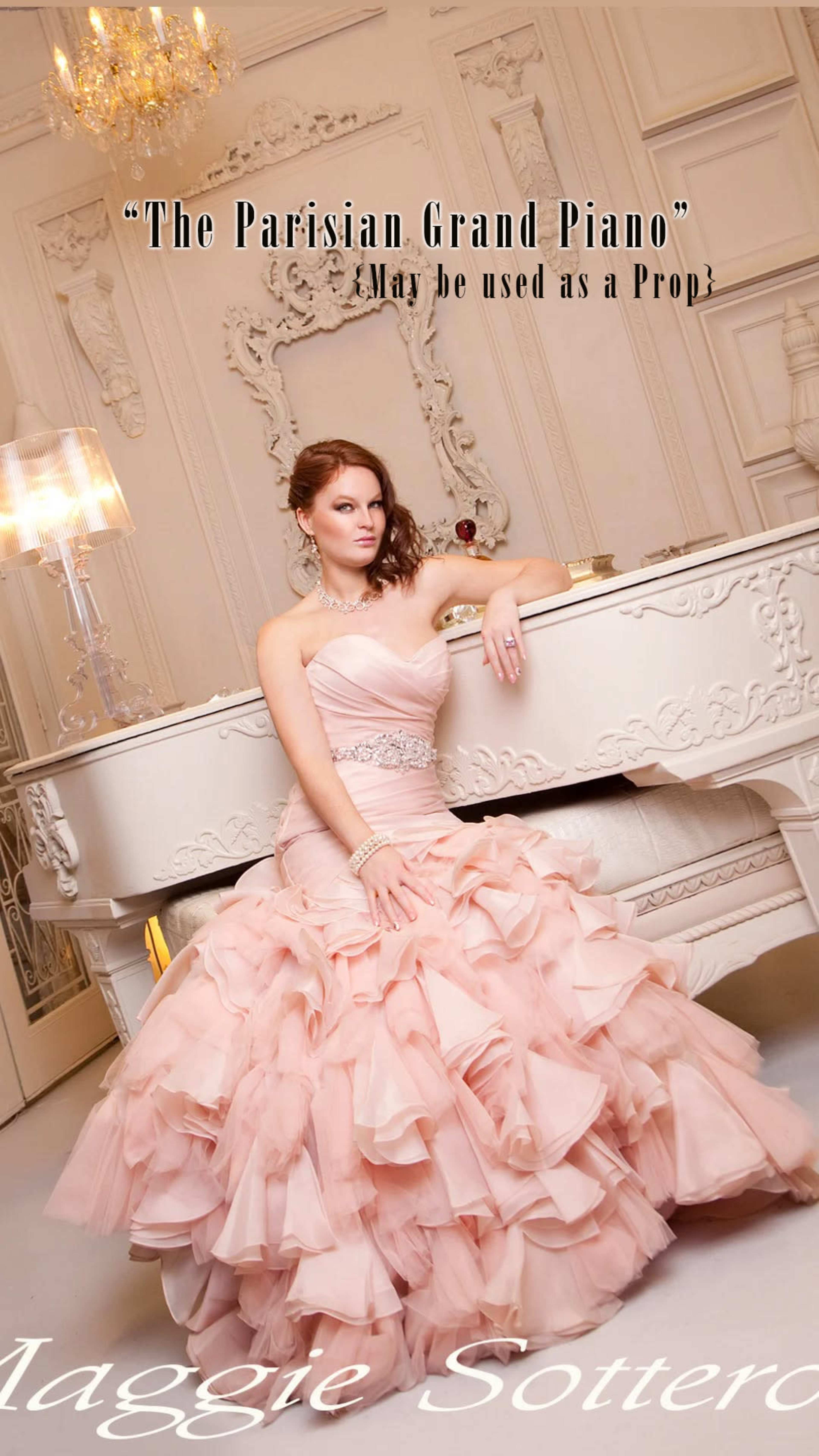 A woman in a layered pink gown leans on a white grand piano in an elegant indoor setting.