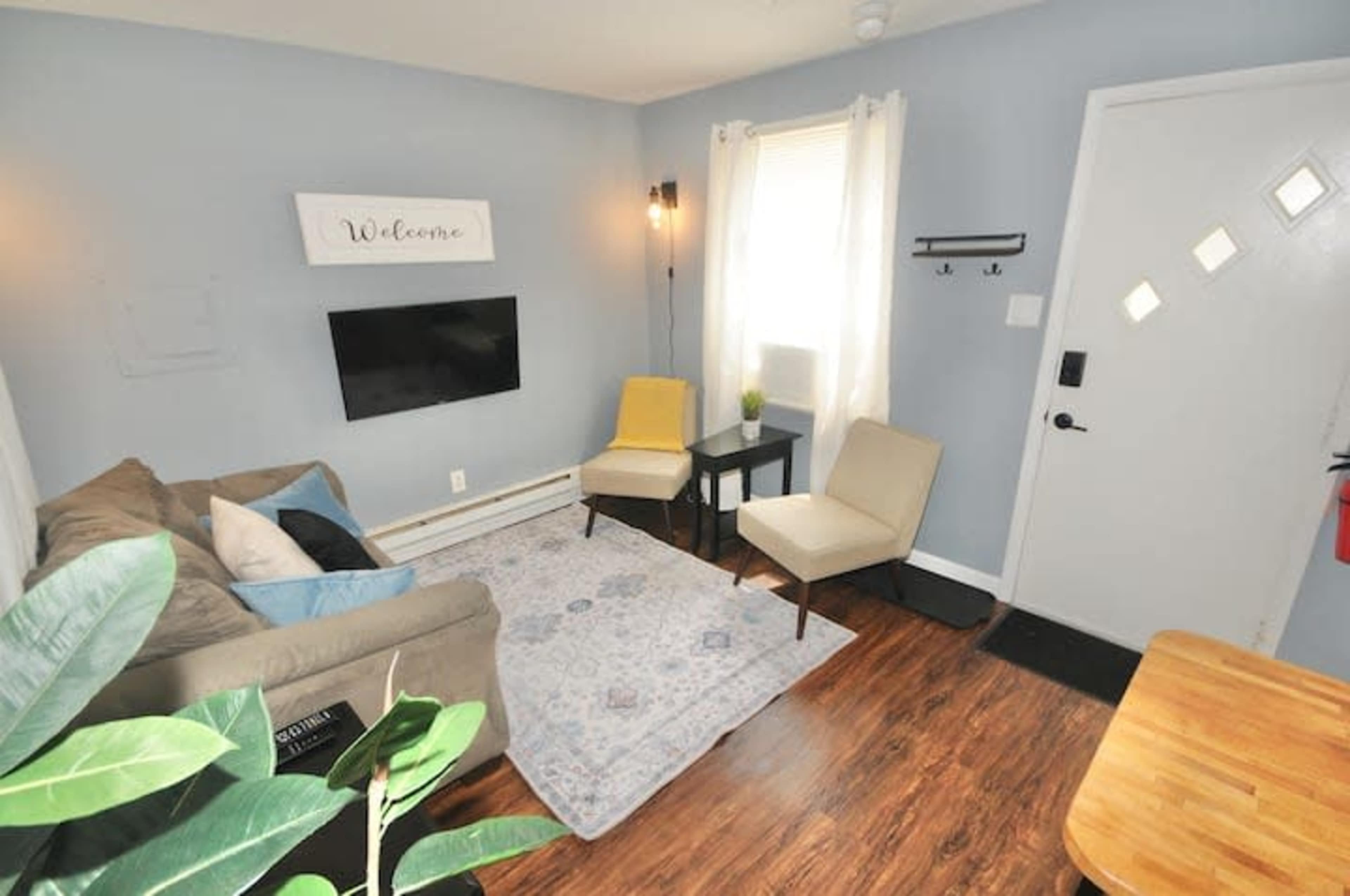 A small living room with a couch, two chairs, a coffee table, a television mounted on the wall, and a door with a window.