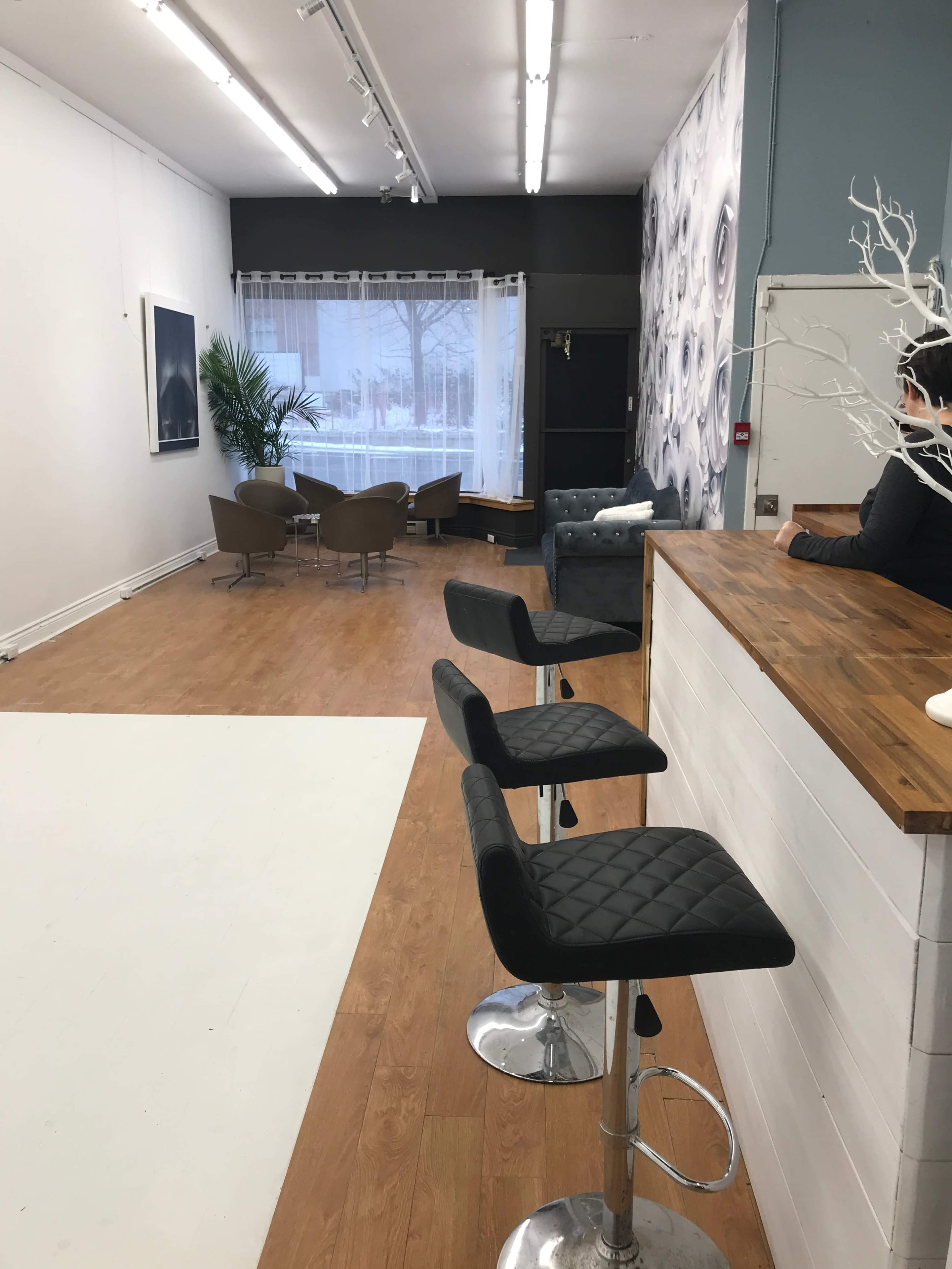 A modern interior space featuring a bar with stools on one side and a seating area with chairs and a large window on the opposite side.