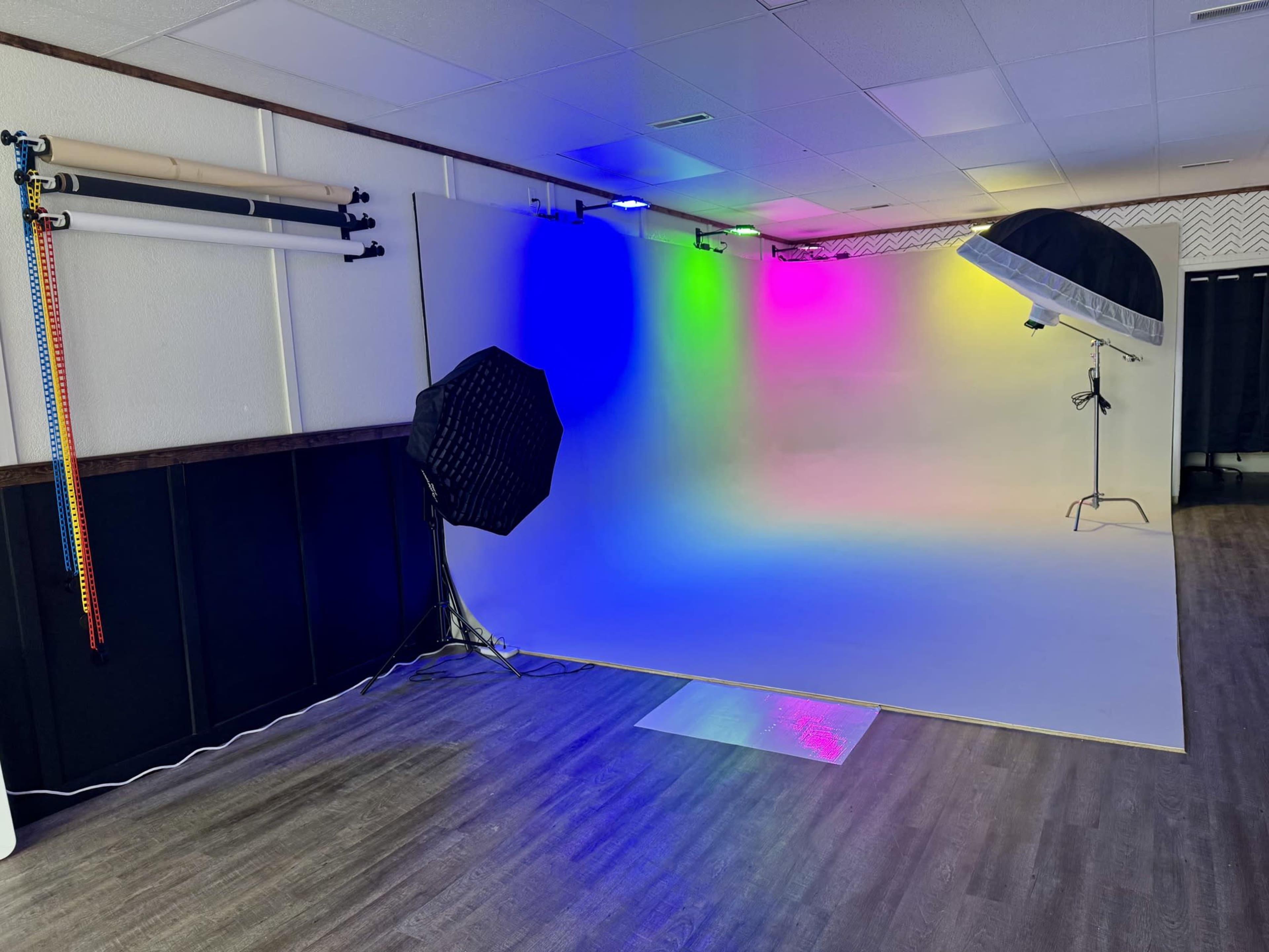 The image shows a photography studio with a colorful light setup, a large umbrella reflector, and a backdrop in a well-lit space.