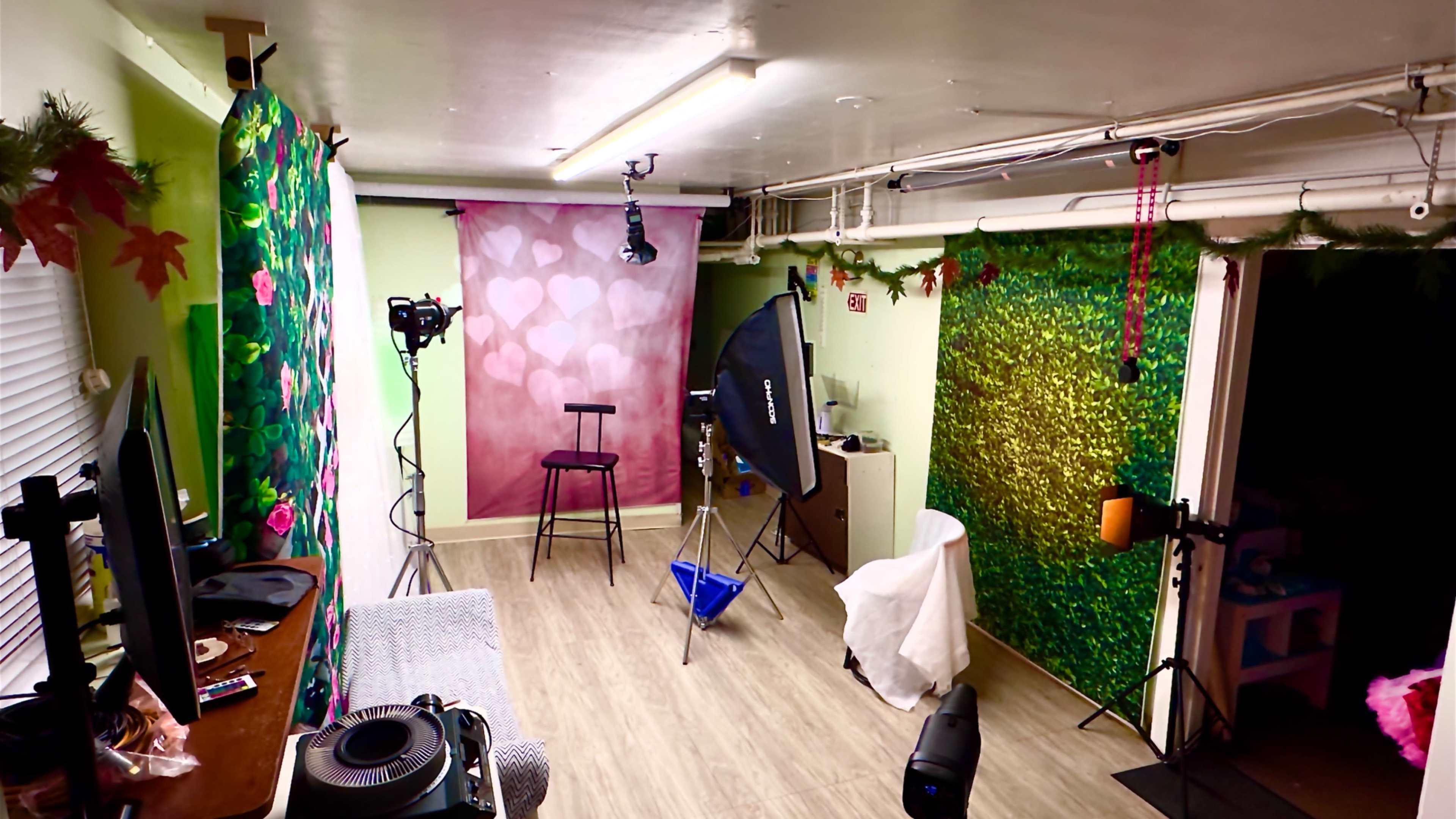 The image shows a small studio space with colorful backdrops, lighting equipment, and a chair set up for photography or video recording.
