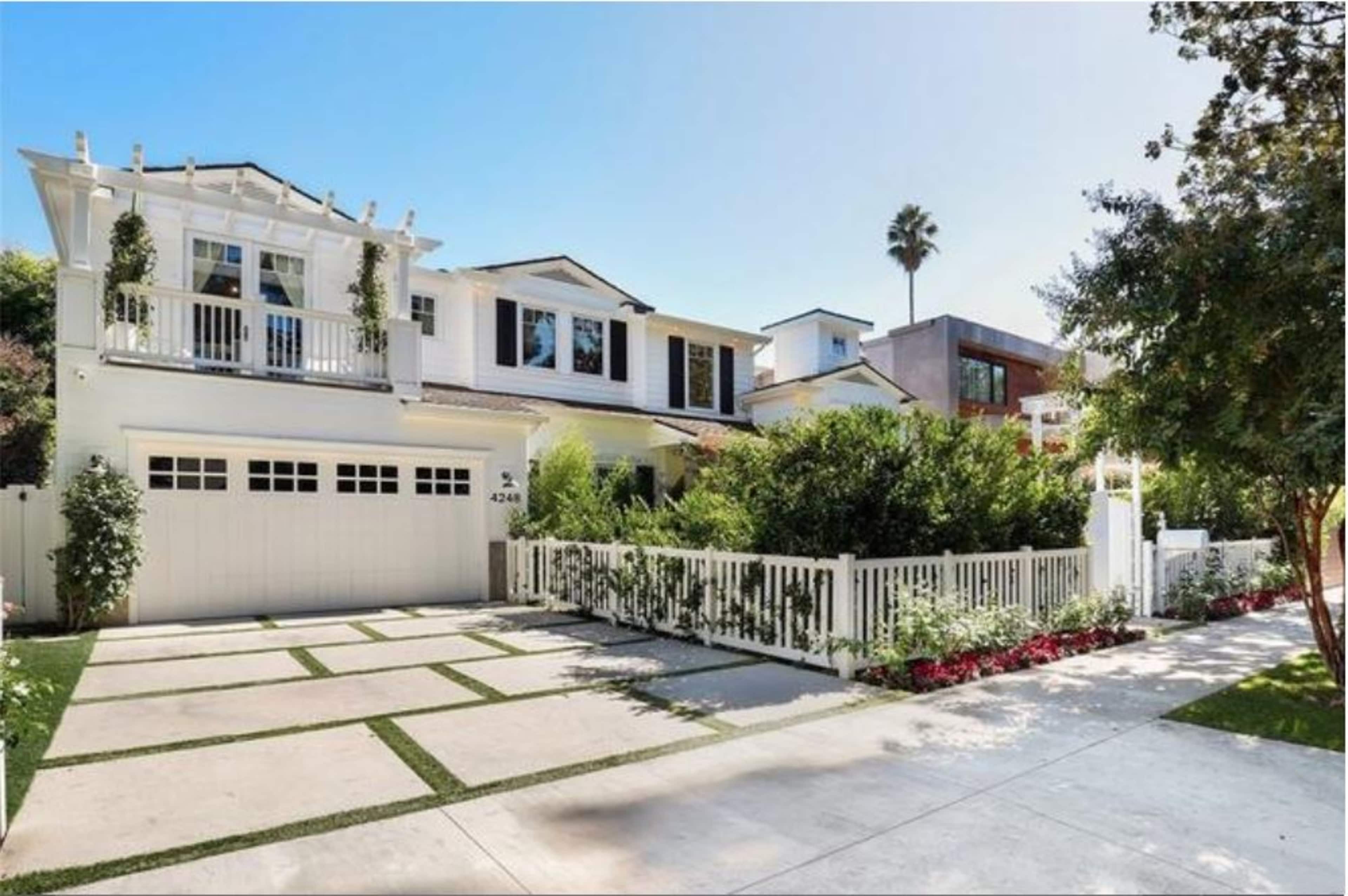 A two-story white house with a landscaped front yard, a driveway, and a picket fence.