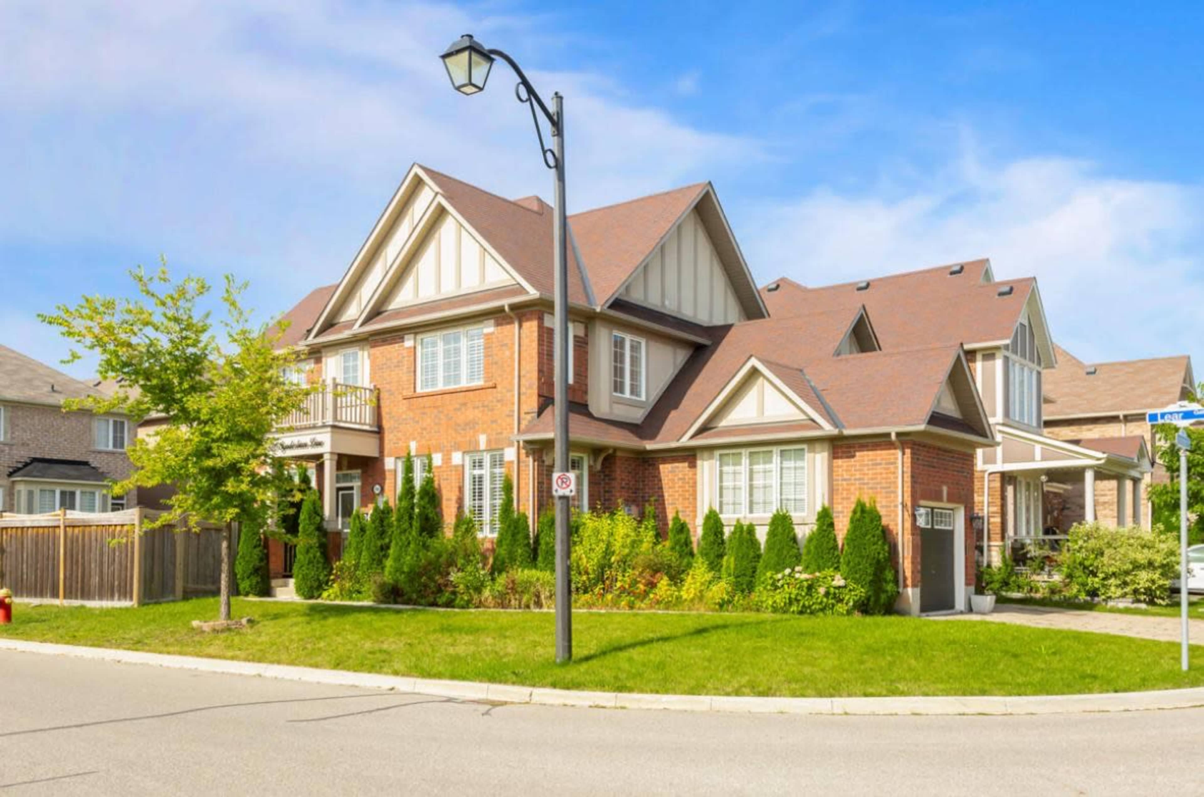 A brick house with a gabled roof and manicured landscaping is situated at the corner of a residential street.
