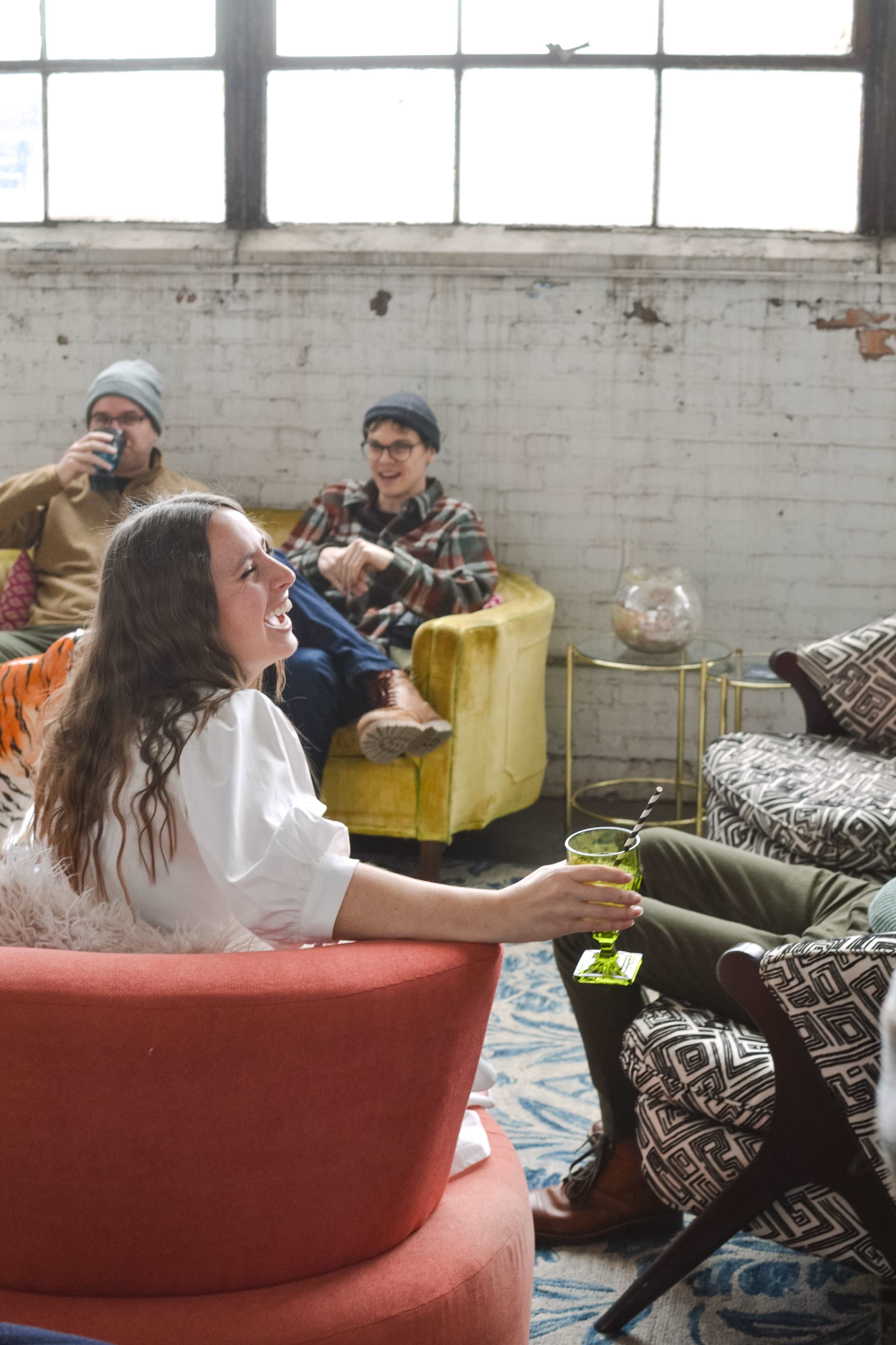 A woman sits in a red chair holding a green drink while three others relax in colorful seating nearby.