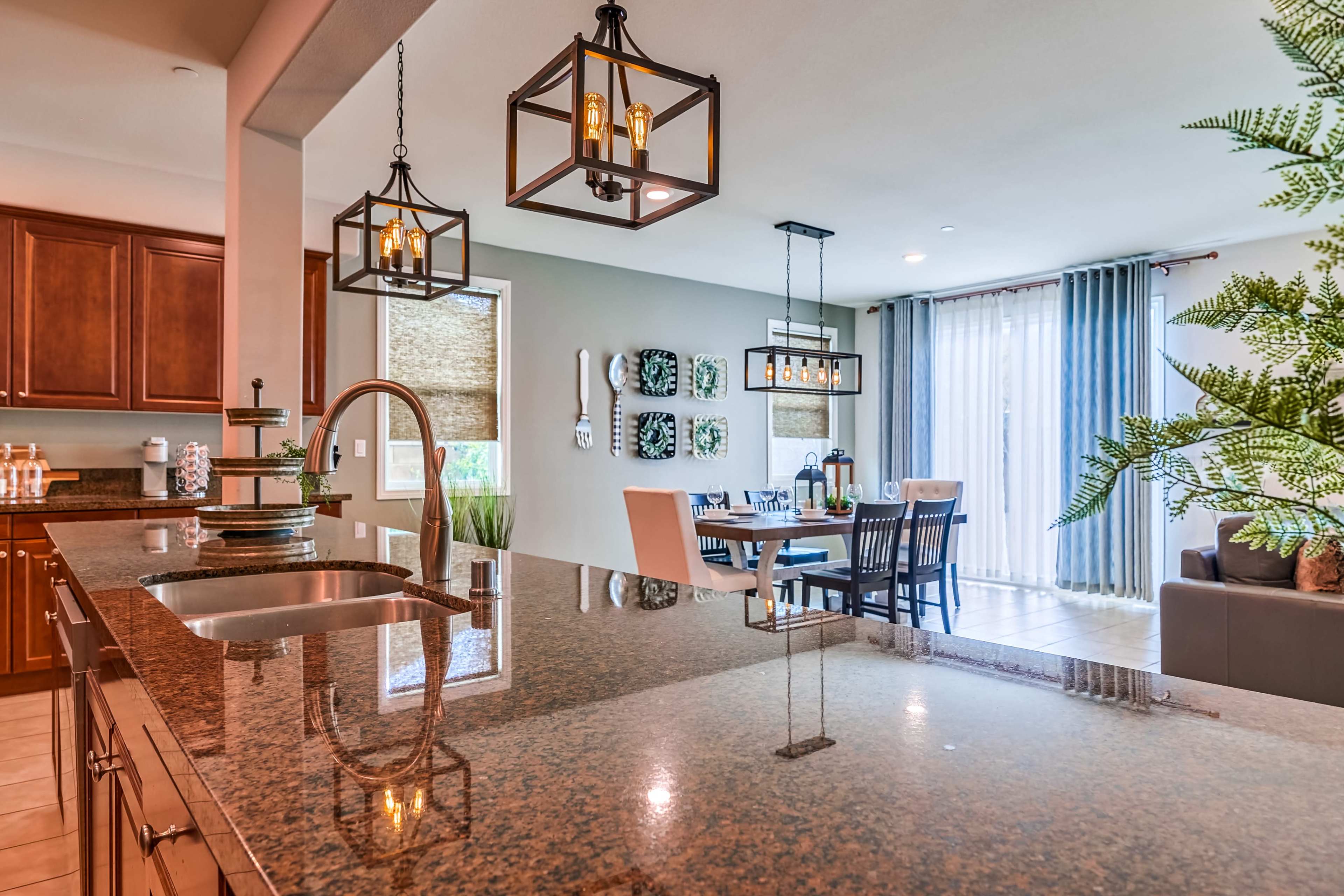 A modern kitchen with dark wooden cabinets, a granite countertop, and an adjoining dining area featuring a table and chairs, illuminated by decorative pendant lights.