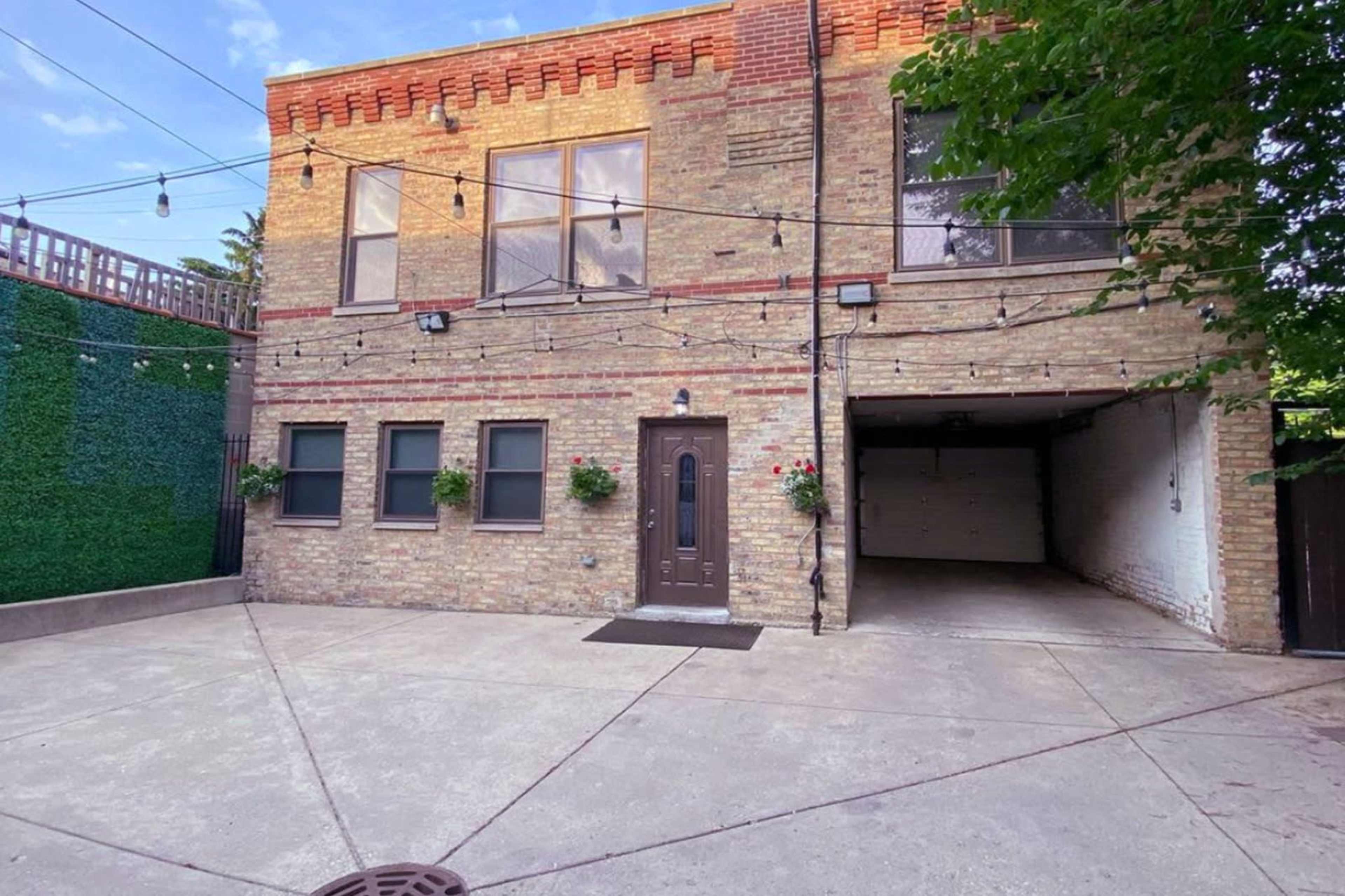 The image shows a two-story brick building with large windows, planters at the entrance, and a garage visible on the ground floor.