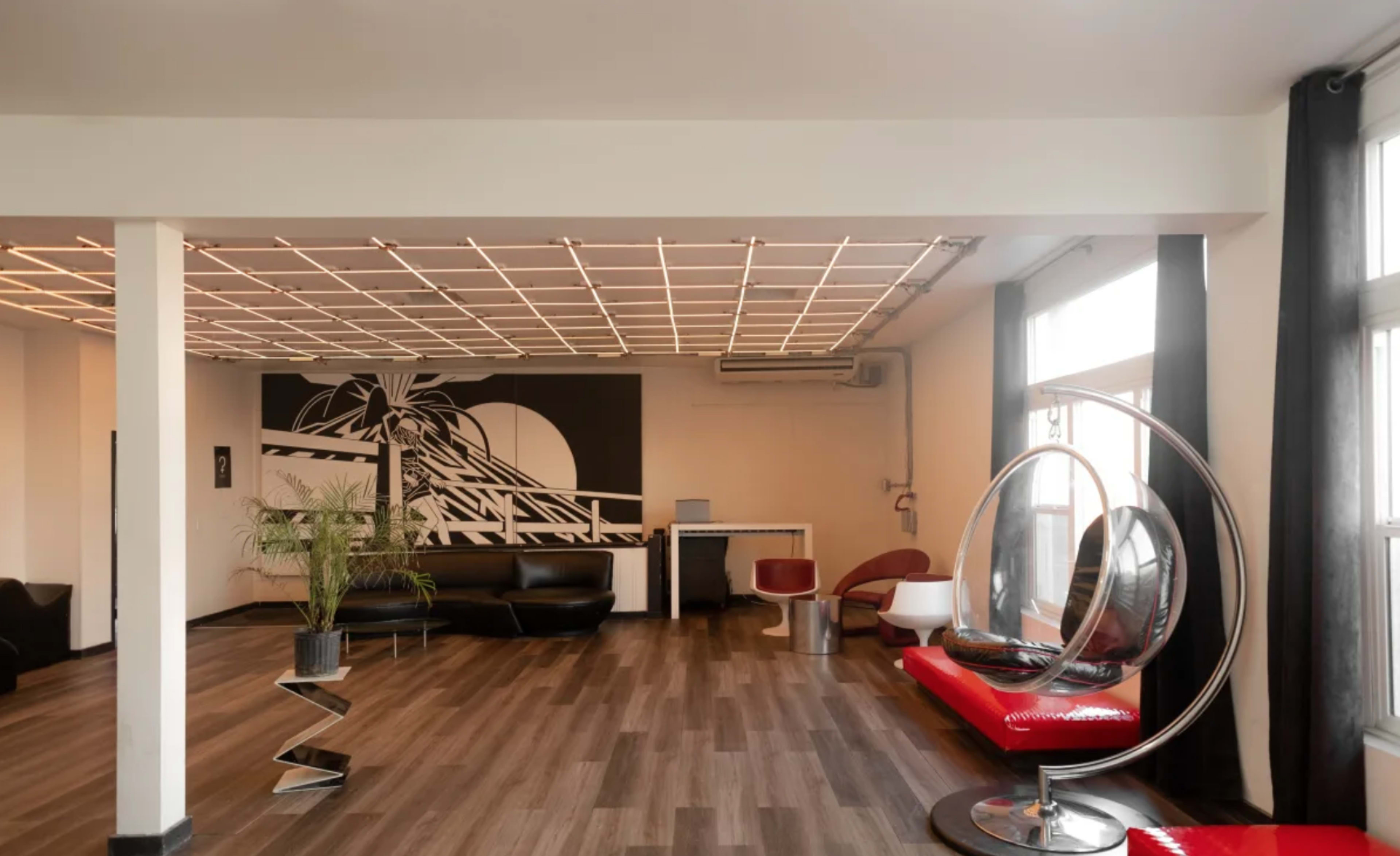 A modern waiting area with sleek furniture, including black and red seating, a large wall mural, and a distinctive hanging chair.