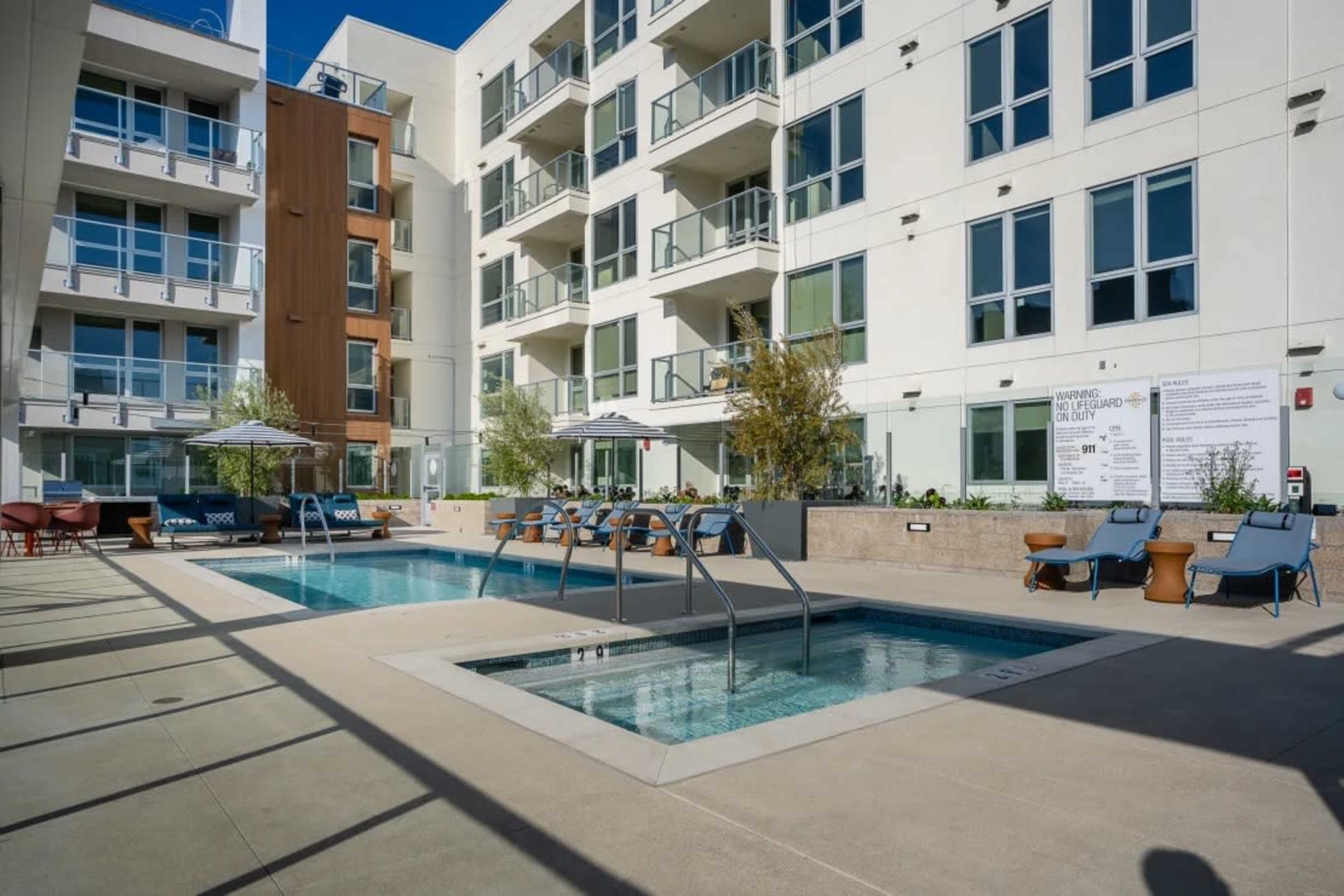 A modern apartment complex with a swimming pool and lounge seating area.