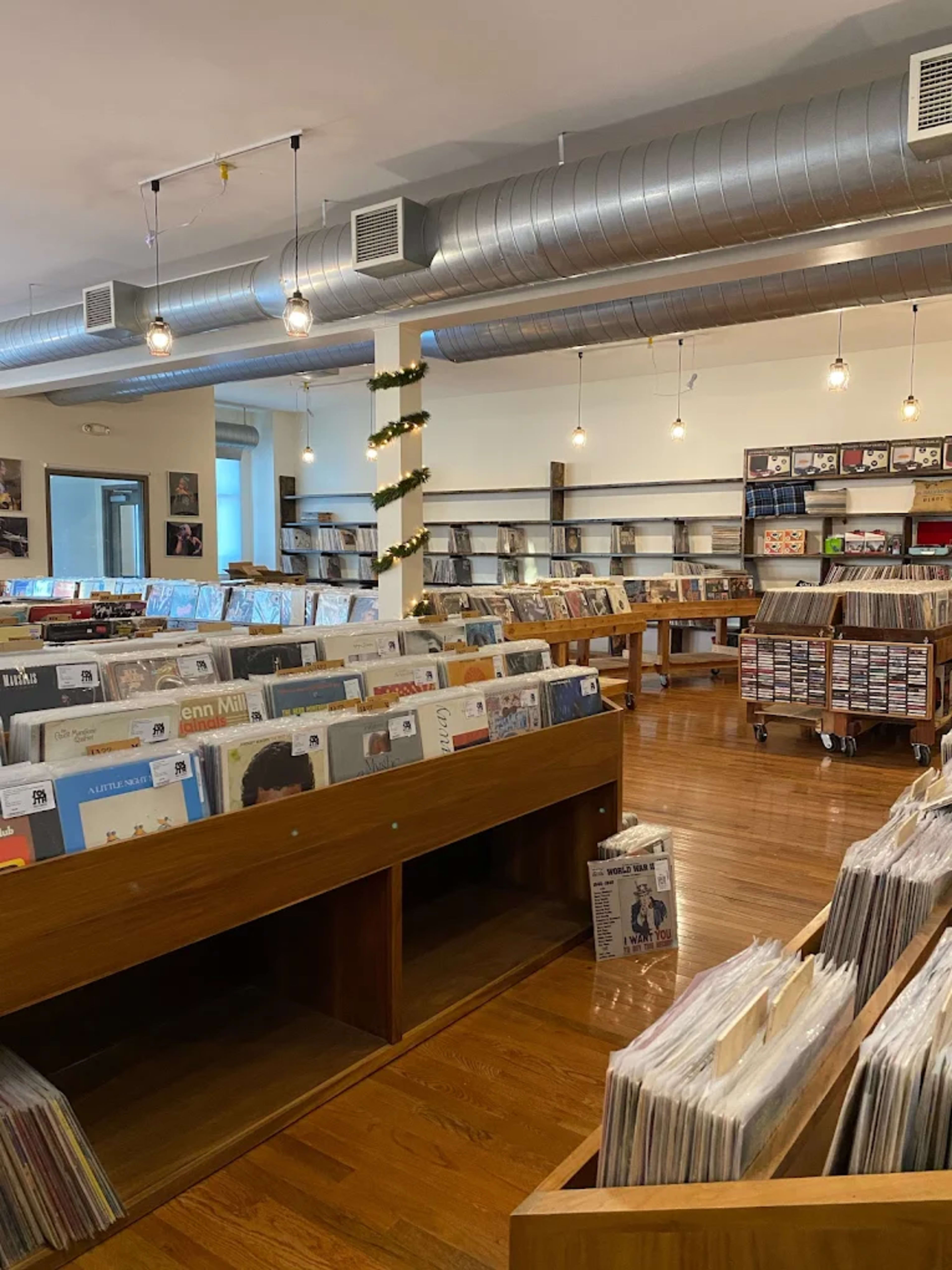 The image depicts a spacious record store with wooden shelves filled with vinyl records and warm lighting overhead.