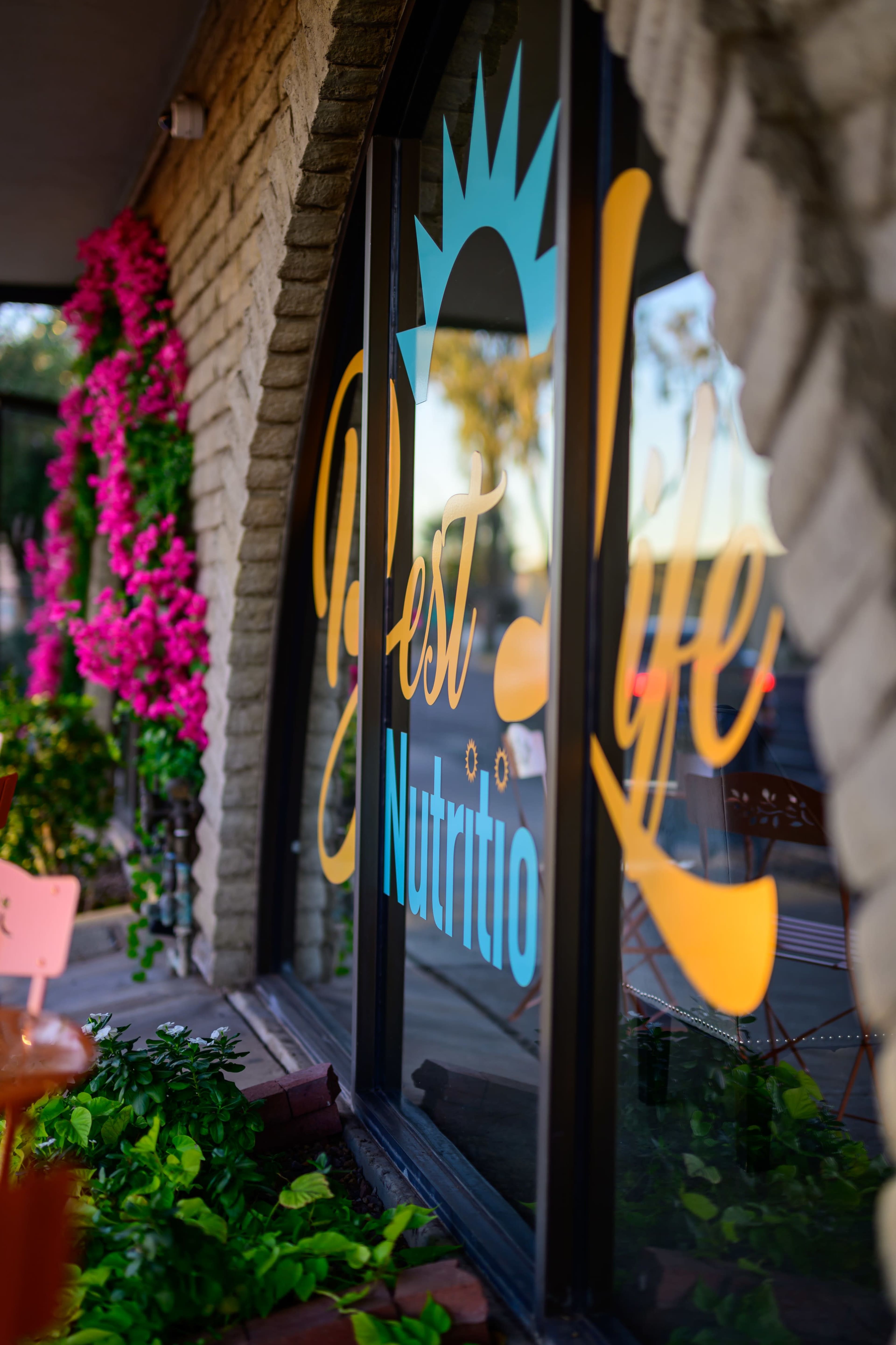 A colorful window sign displays the words "Best Life Nutrition" against a backdrop of pink flowers and greenery.