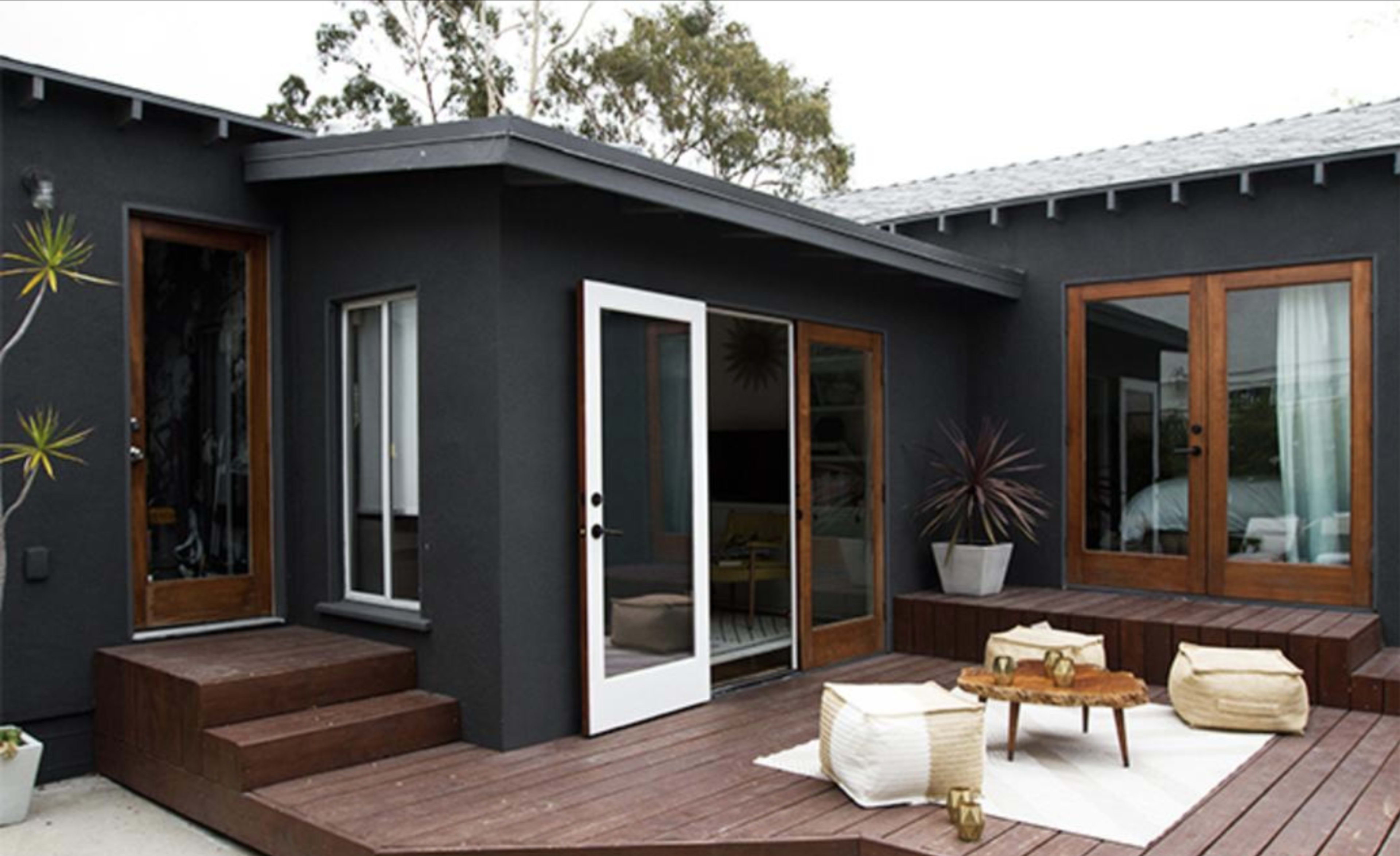 A modern outdoor patio area with wooden steps leading up to a home featuring large glass doors and a small table surrounded by seating.