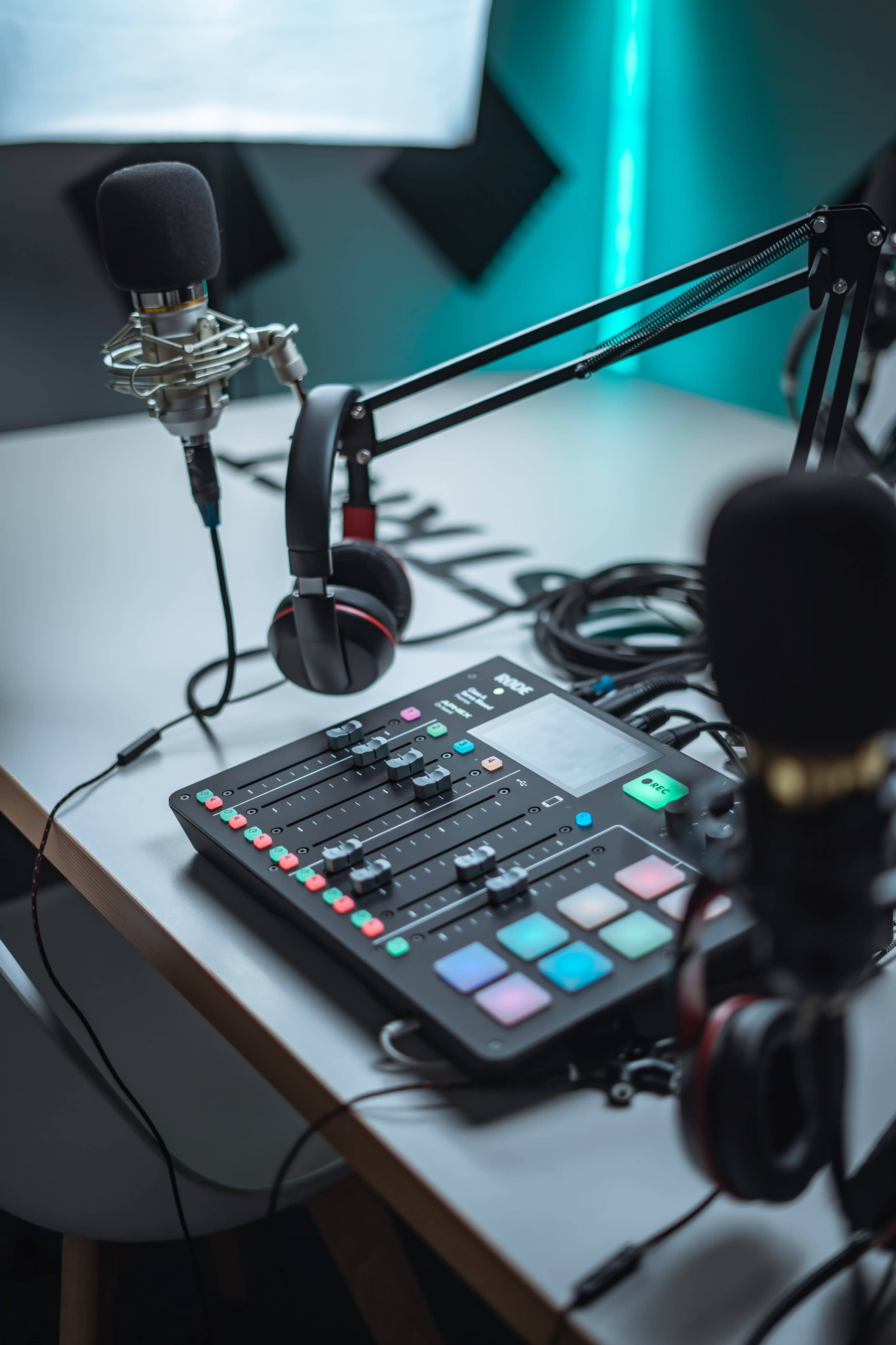 A podcasting setup features a table with a sound mixing console, two microphones on stands, and headphones.