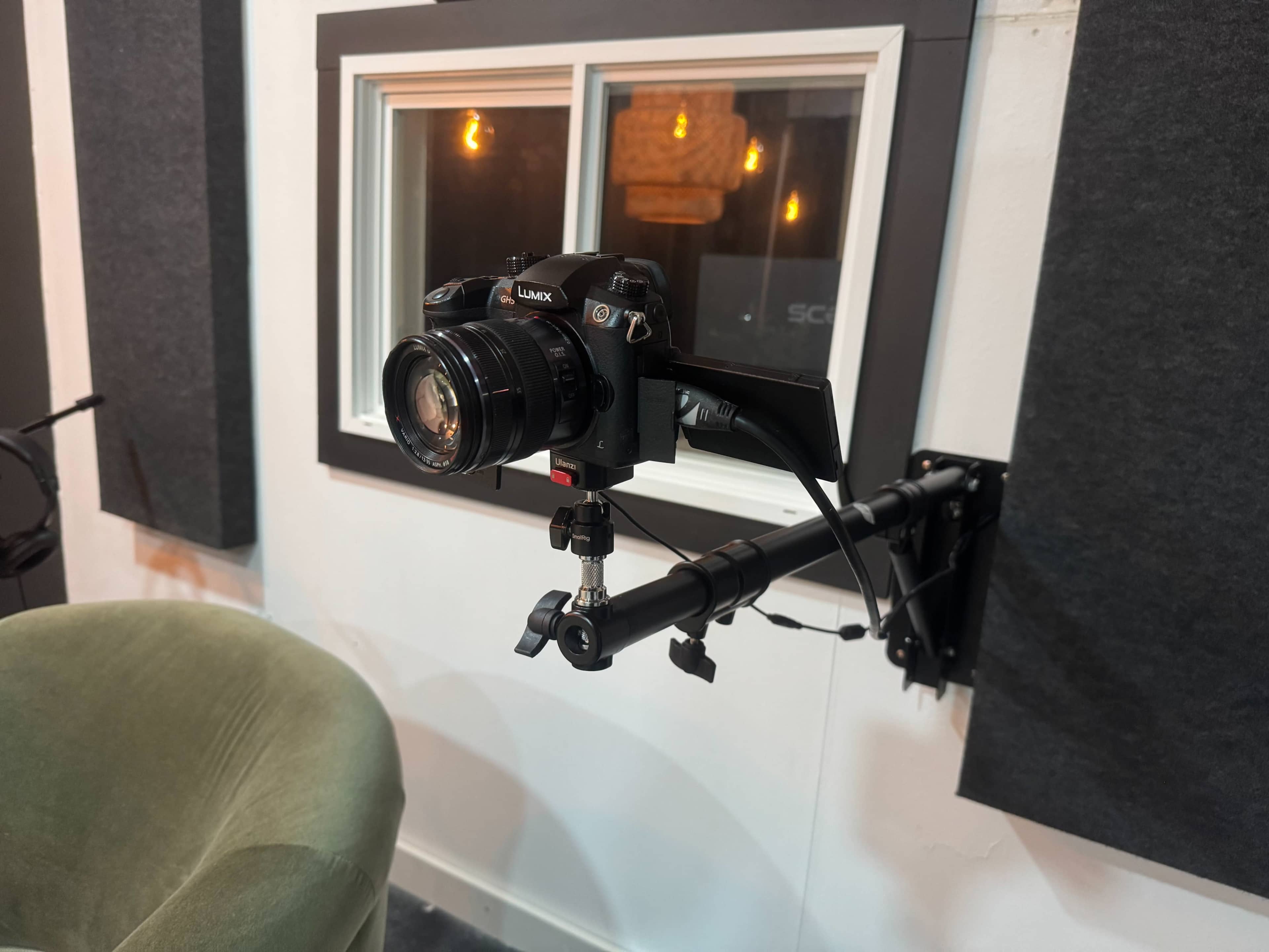 A camera is mounted on an adjustable arm, positioned in front of a window in a recording studio.
