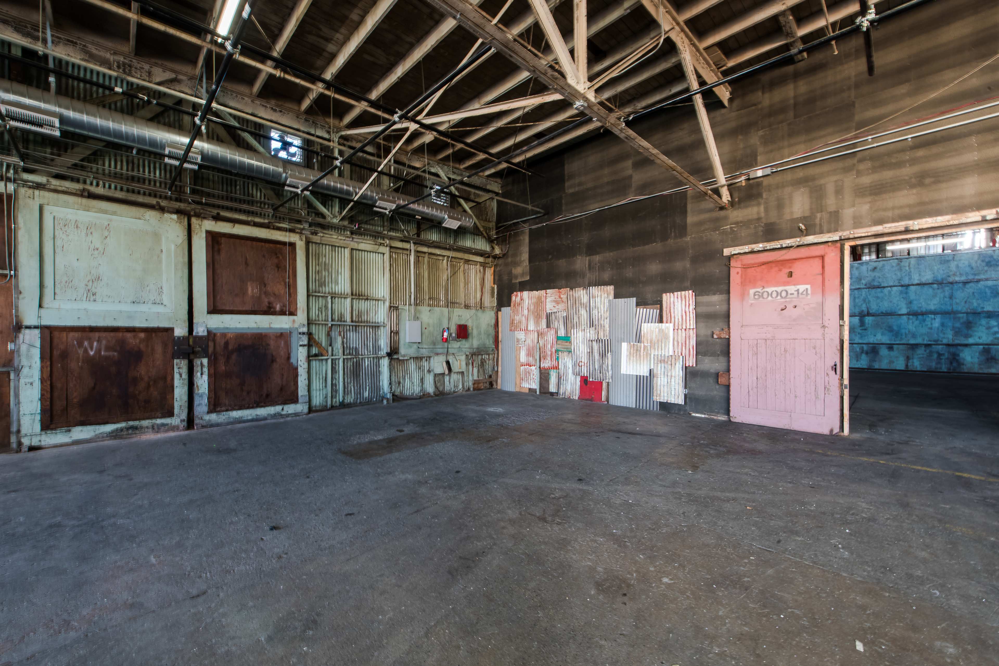 The image shows an industrial space with weathered walls, multiple large doors, and a colorful display of arranged panels on one side.