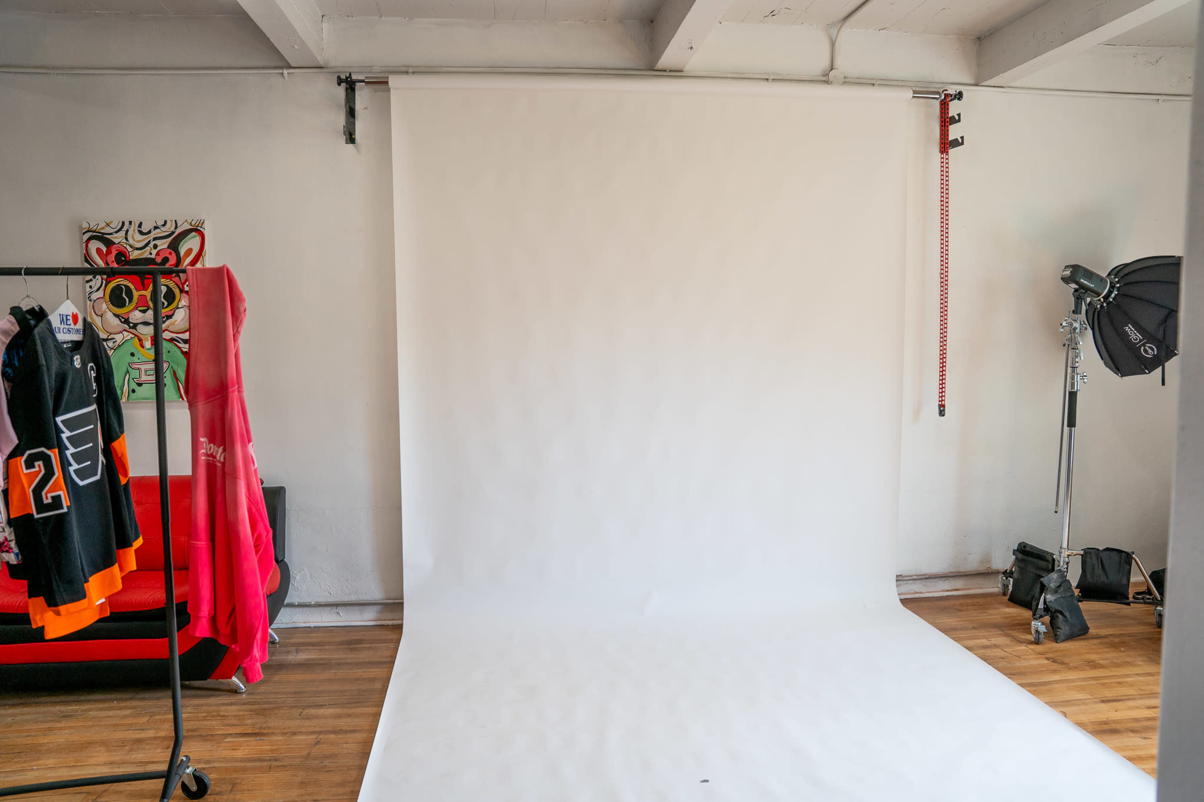 The image shows a photography studio with a plain white backdrop, a clothing rack holding sports jerseys, and lighting equipment in the corner.