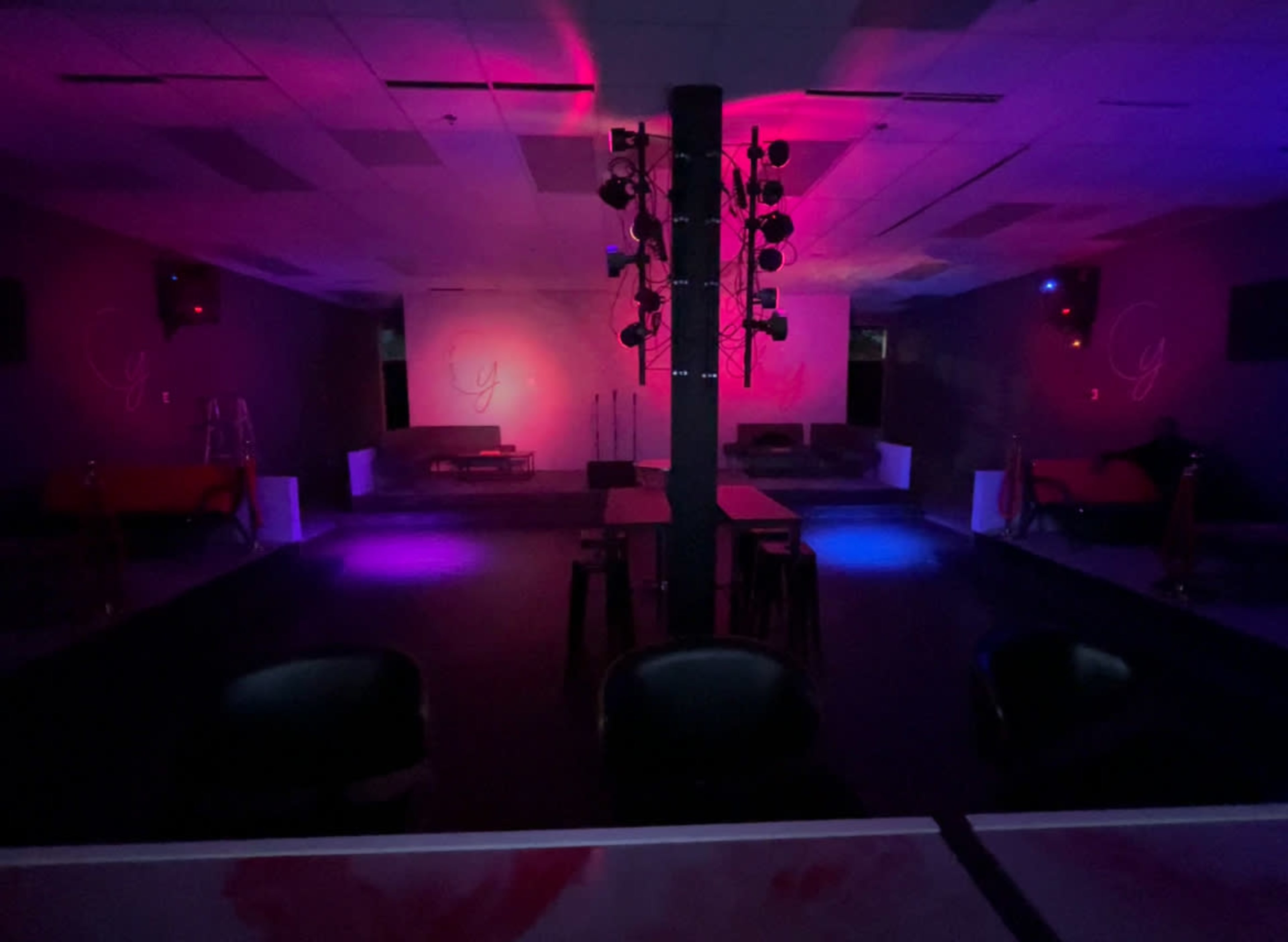 The image shows an empty nightclub interior with dim lighting and a stage featuring a spotlight setup.