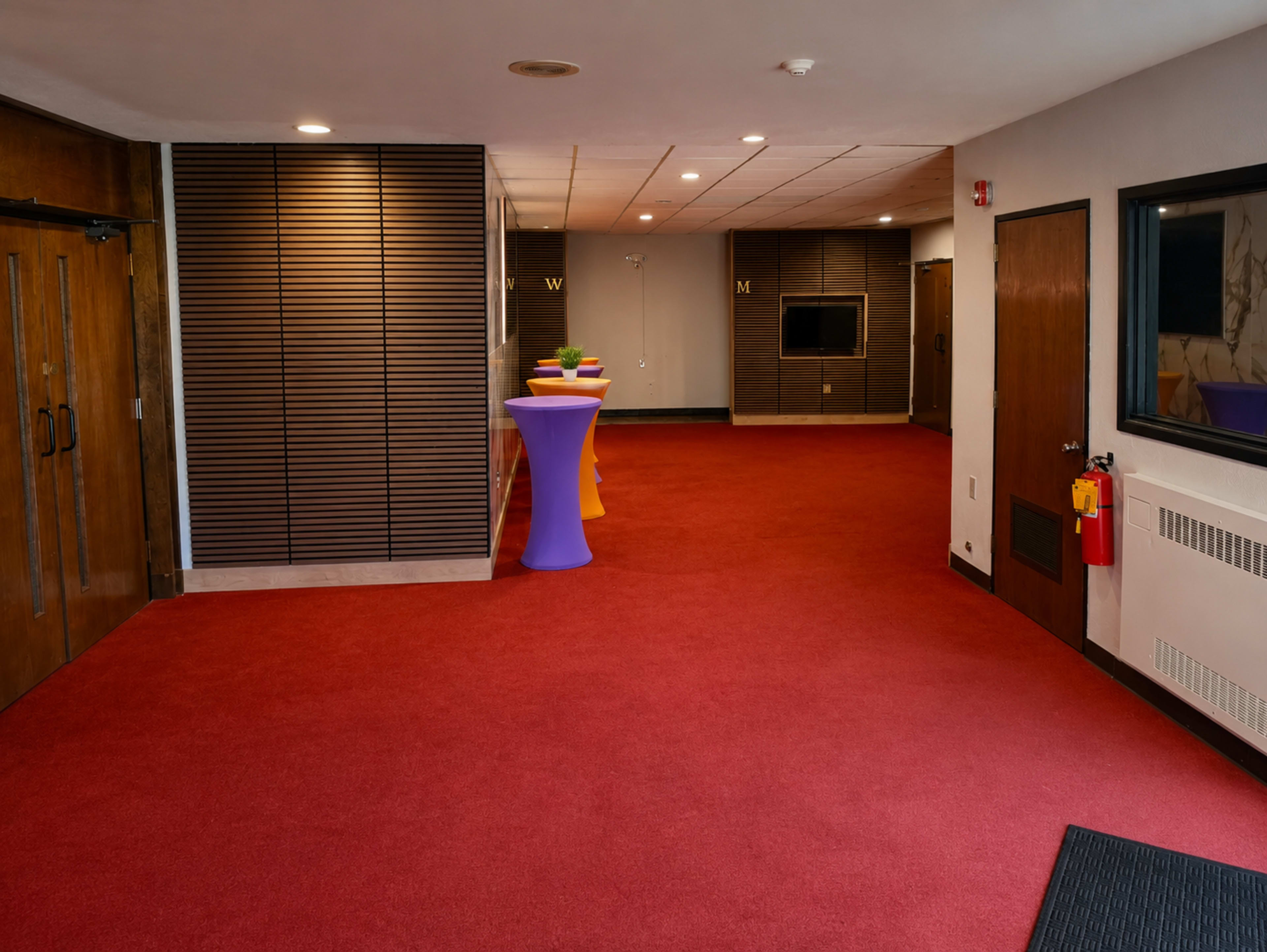 The hallway features a red carpet, wooden doorways, and a table with a colorful tablecloth set against a paneled wall.