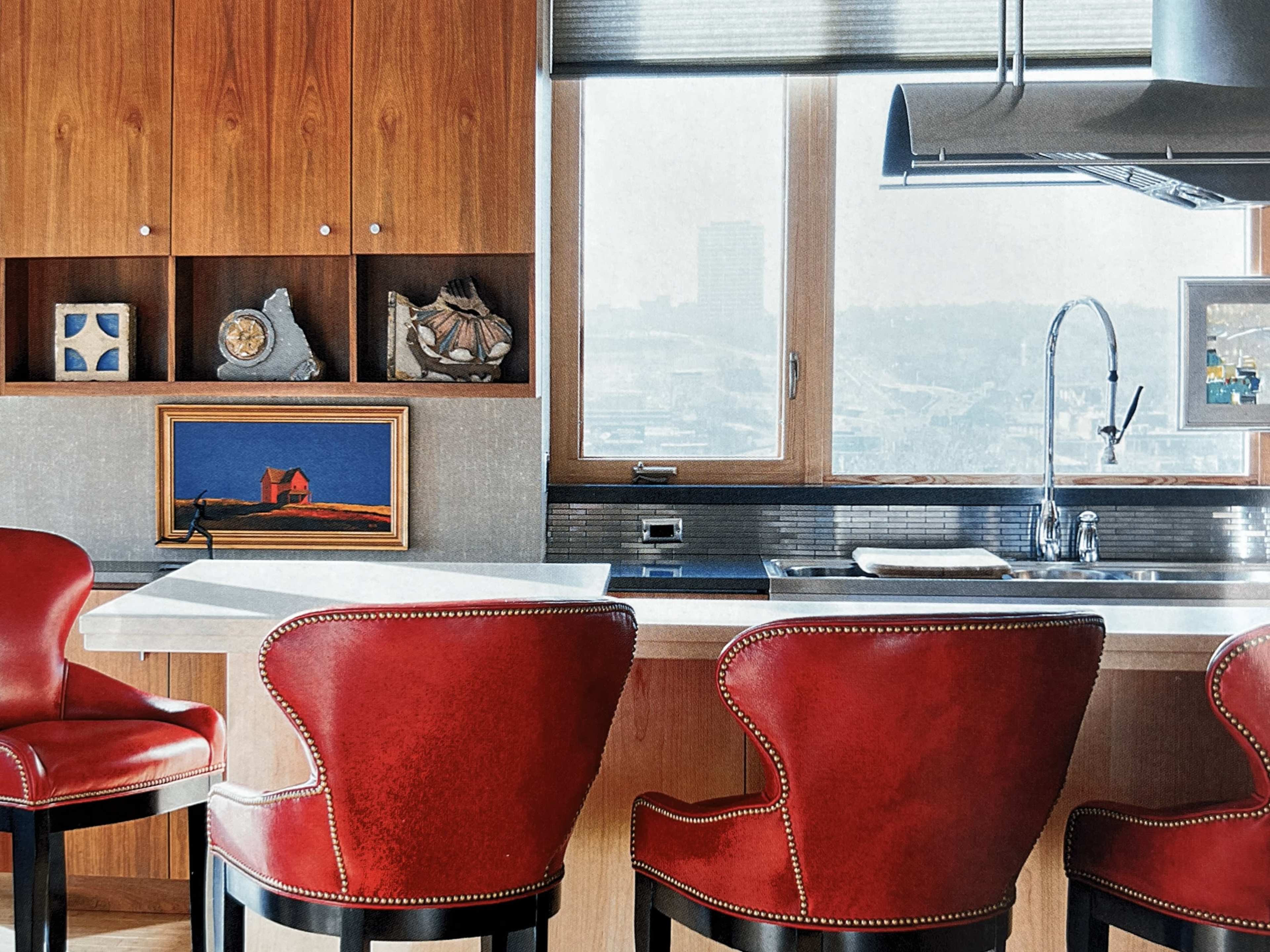 The image shows a modern kitchen with wooden cabinetry, a stainless steel sink, and three red-upholstered bar stools.