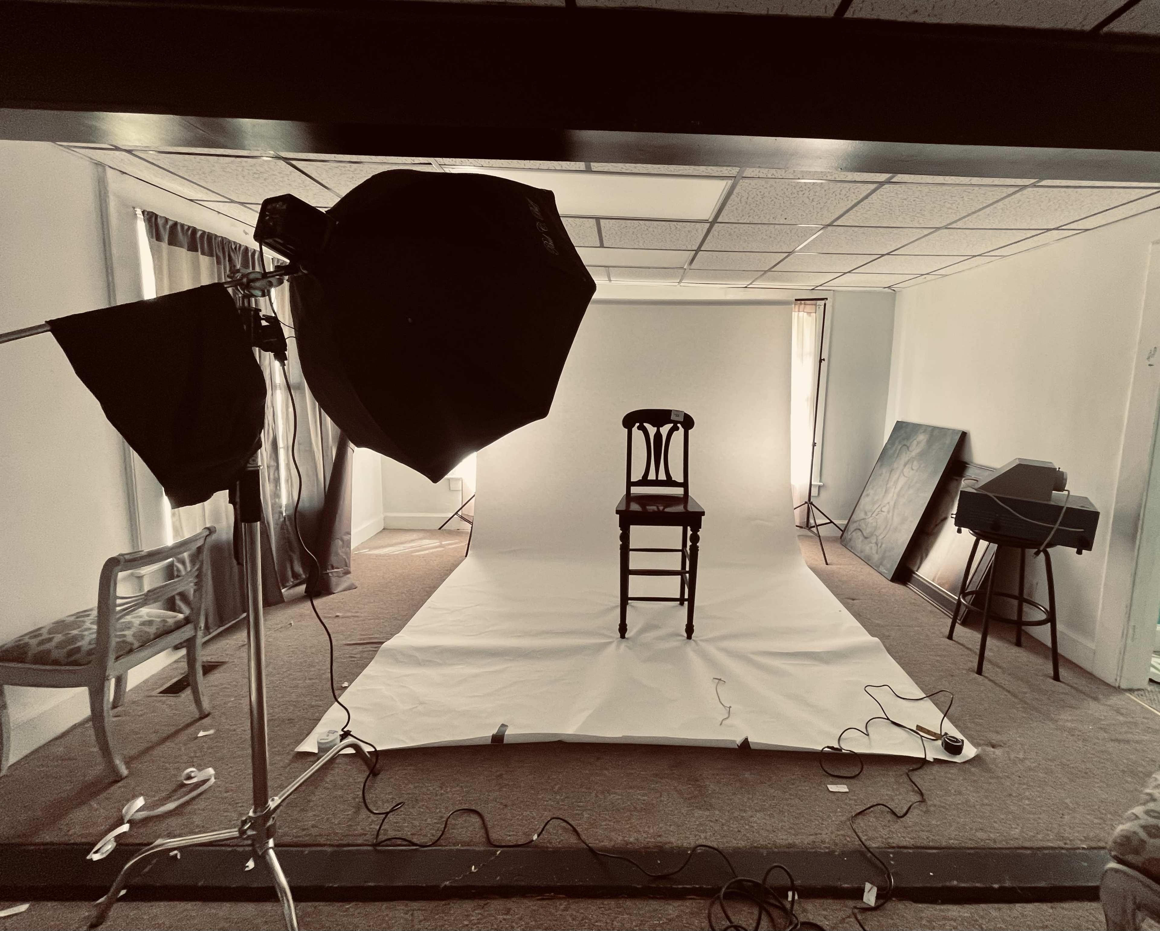 A photography setup features a chair positioned on a white backdrop, with lighting equipment and cables around it.
