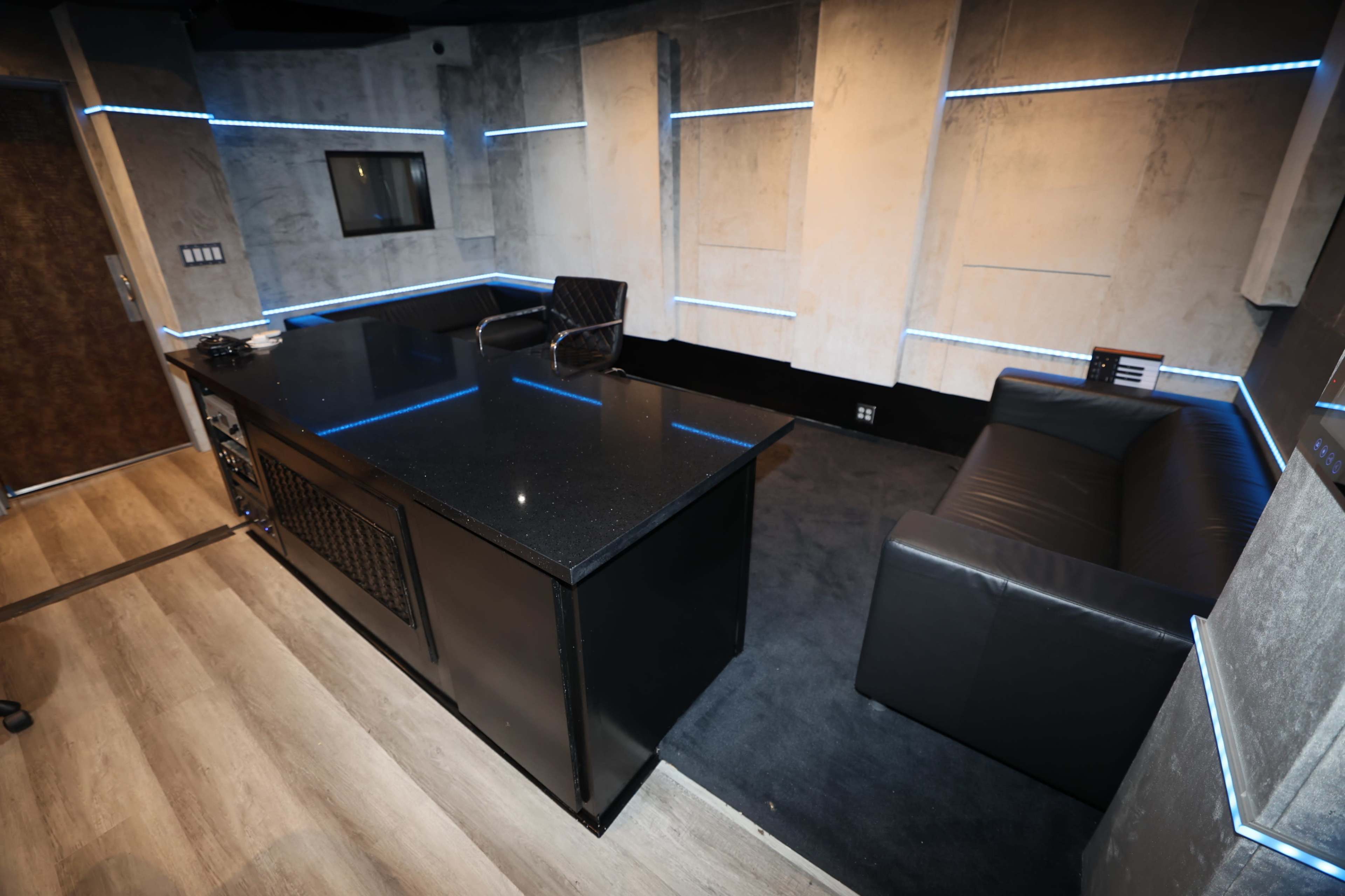 The image depicts a modern interior space featuring a black countertop, a chair, a black sofa, and illuminated wall sections.