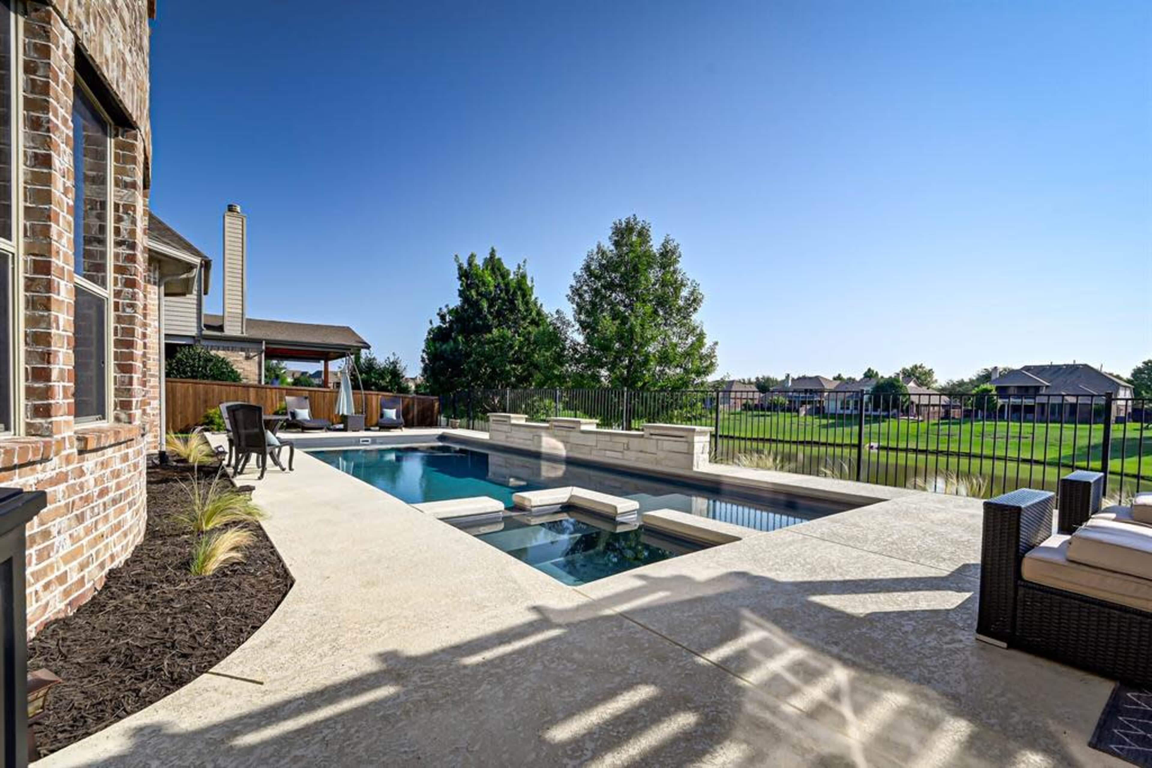 A spacious backyard with a rectangular swimming pool surrounded by a concrete deck and a view of well-maintained lawns and houses in the background.