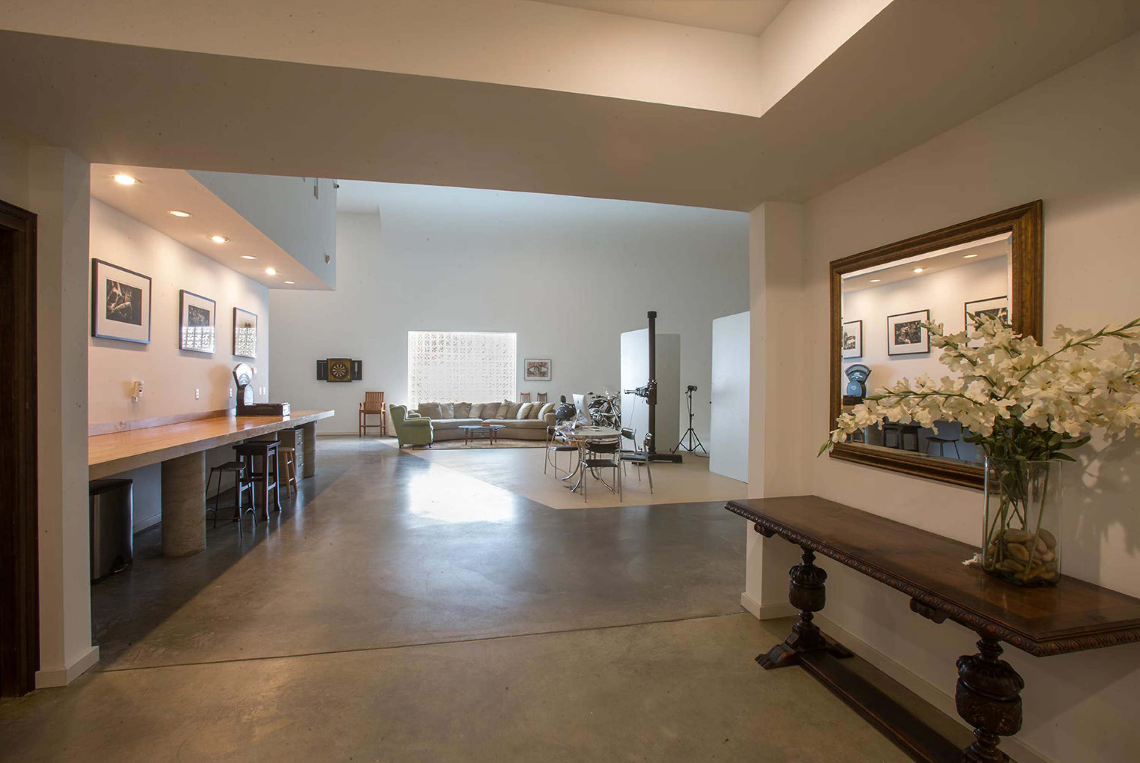 An open-concept living space featuring a bar area on the left, a seating area in the background, and a console table with a vase of flowers in the foreground.