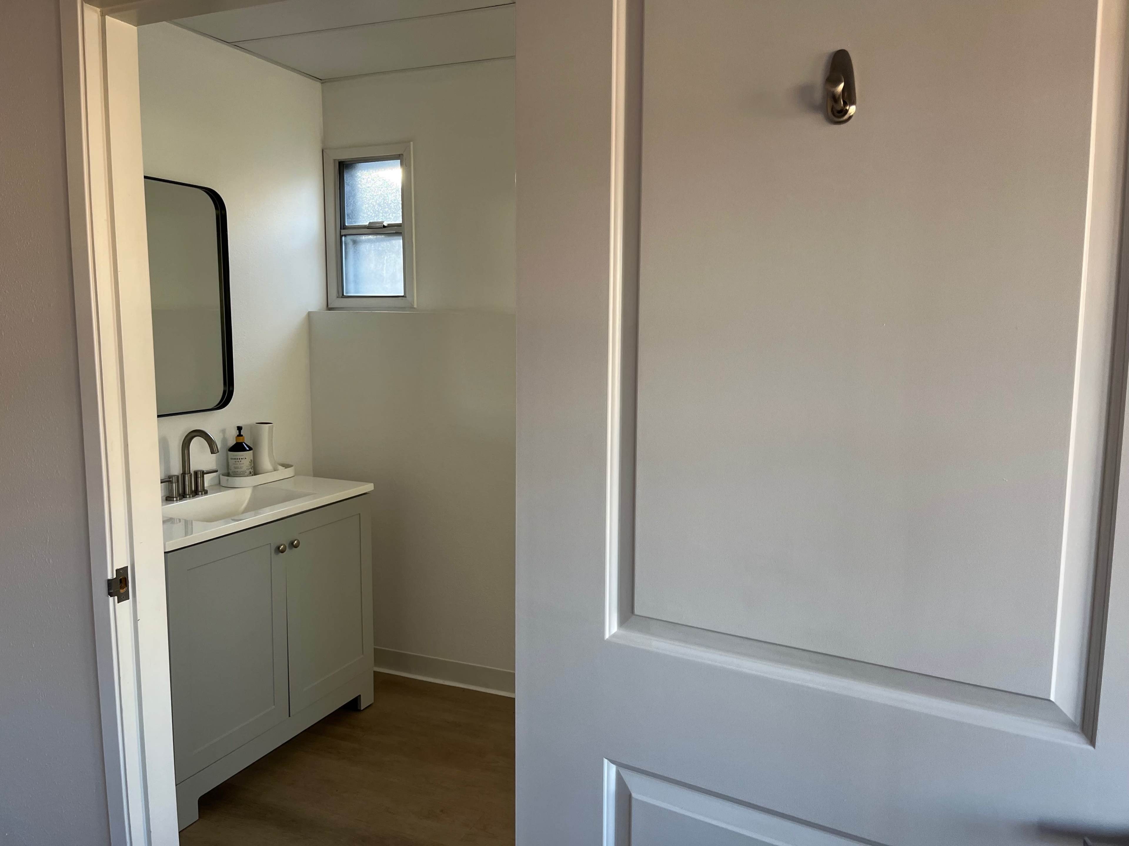 A modern bathroom with a small sink, a mirror, and a door partially open to another room.
