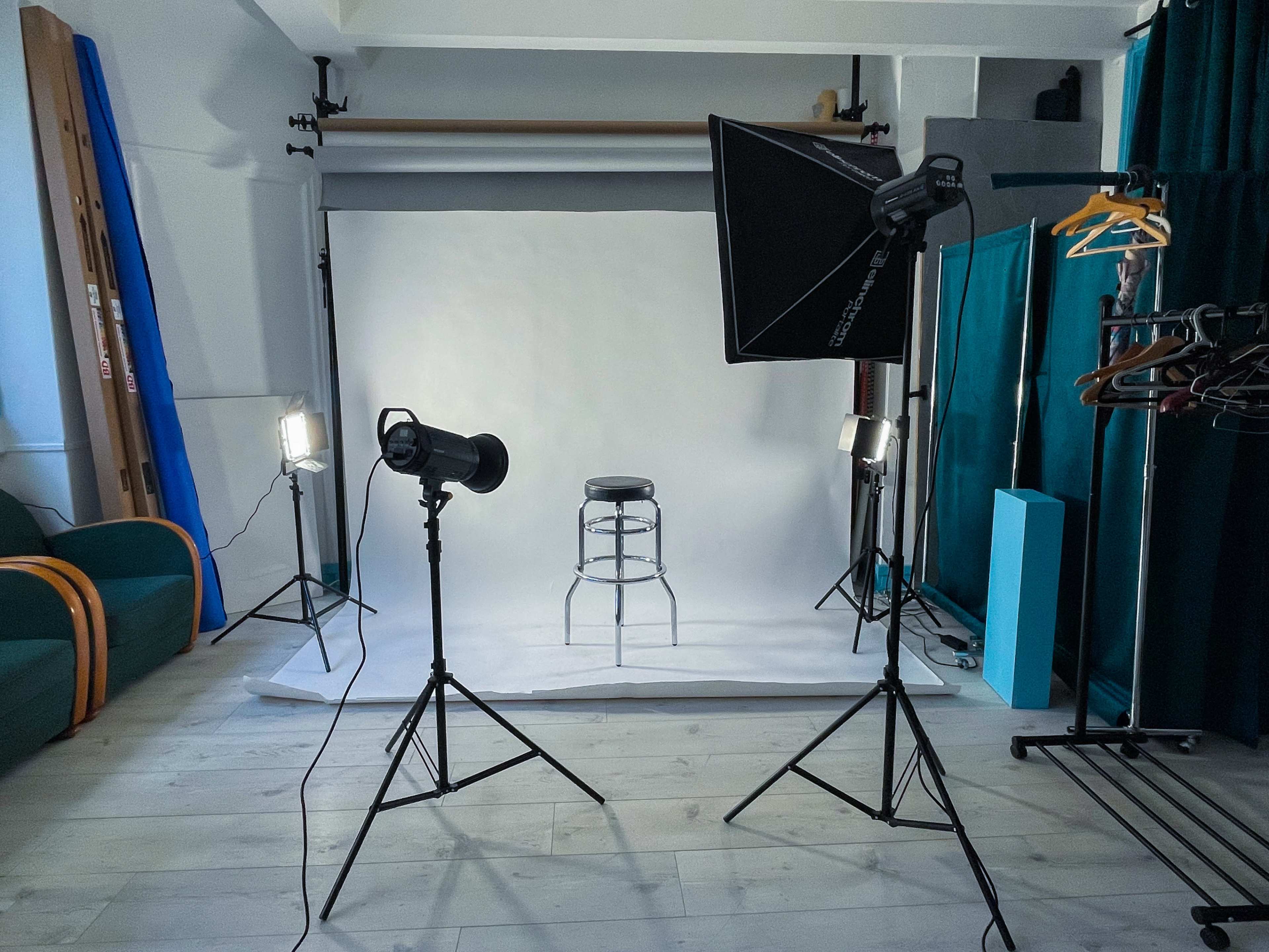 A photography studio is set up with two lights, a stool in the center, and a white backdrop.