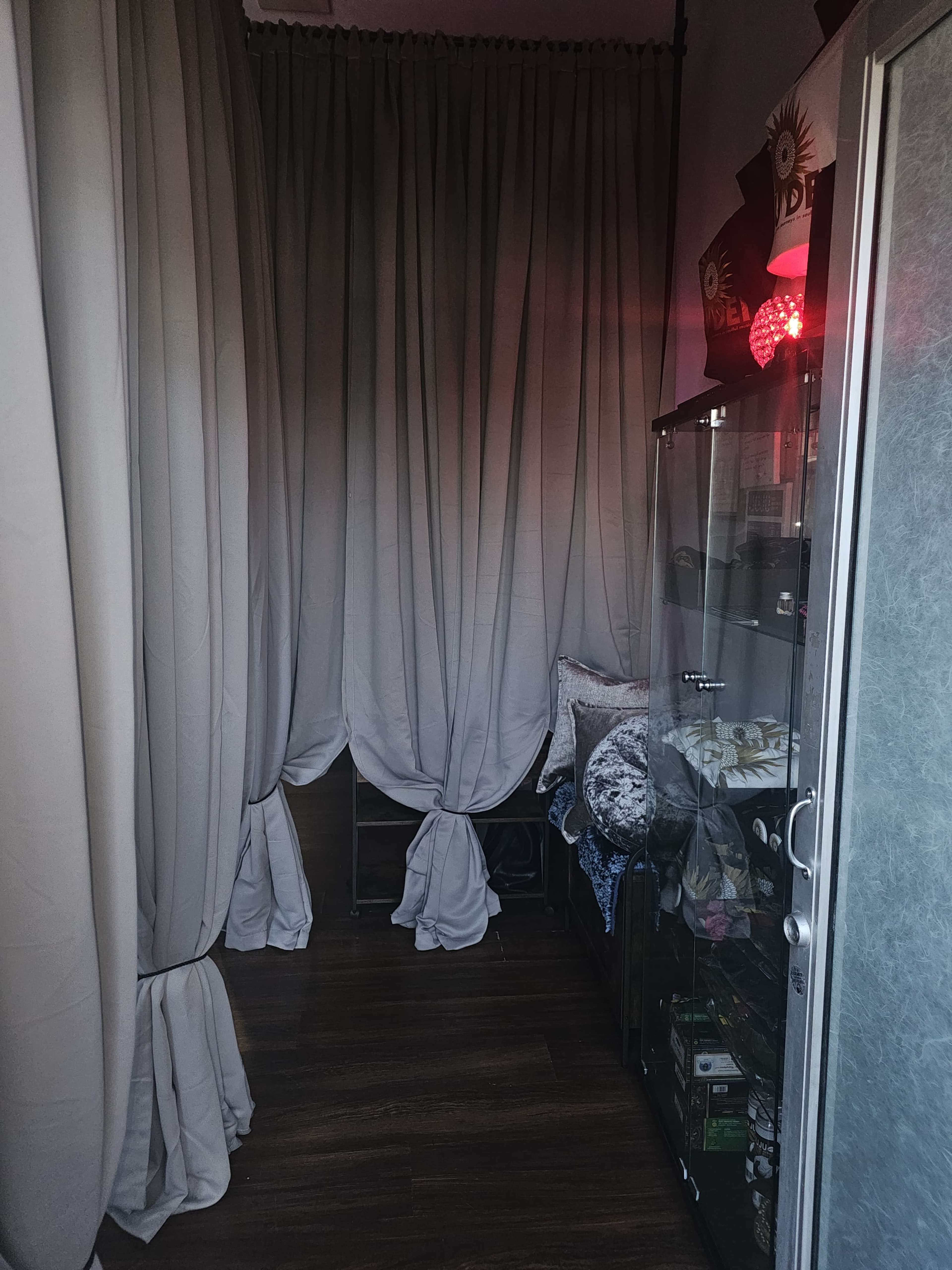 A narrow hallway with grey curtains on one side and a glass display case on the other, containing various items.