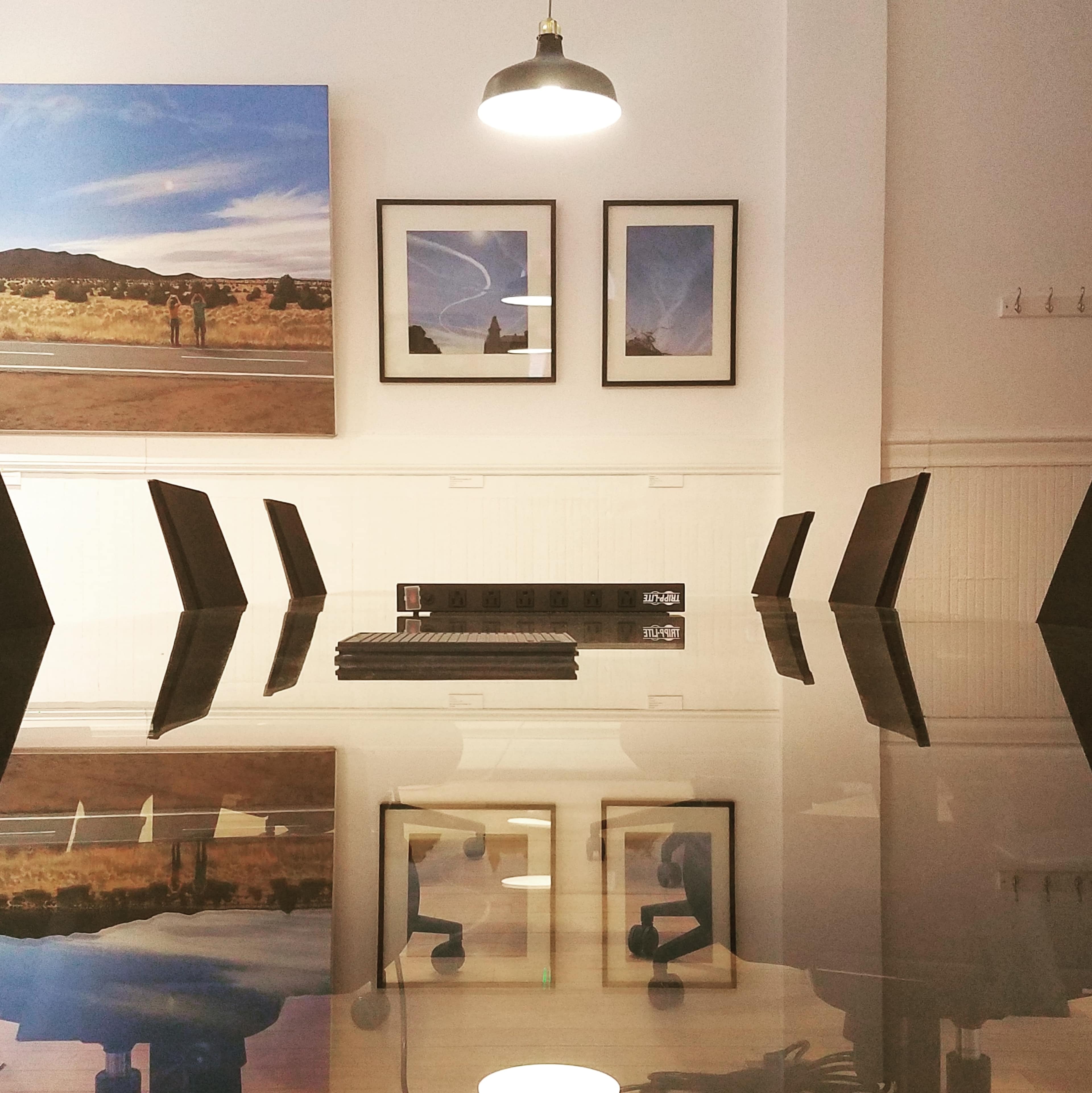A modern conference room features a long glass table, black chairs, framed artwork on the walls, and a ceiling light illuminating the space.