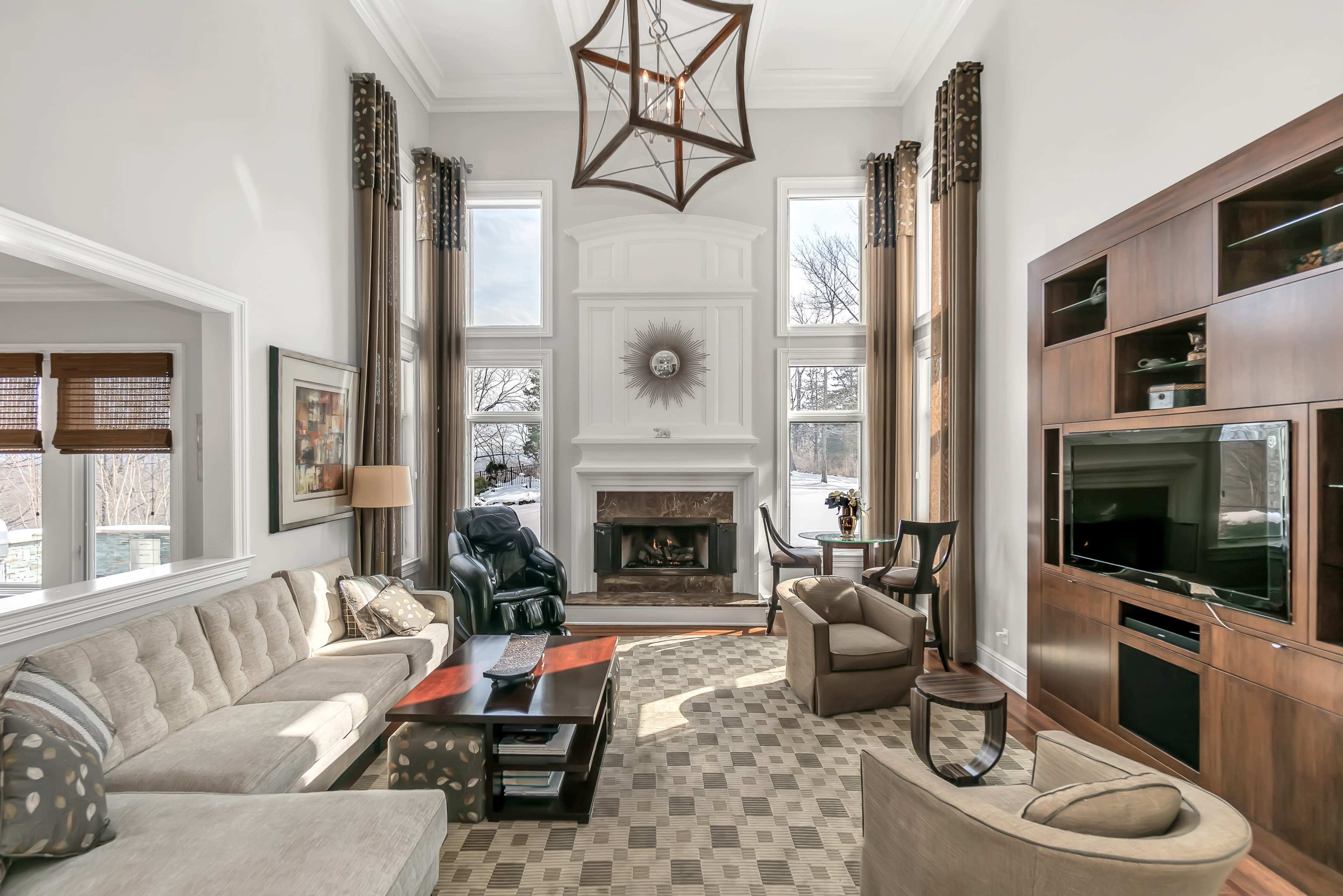 A spacious living room features a large window, a fireplace, a sectional sofa, and a mounted television.