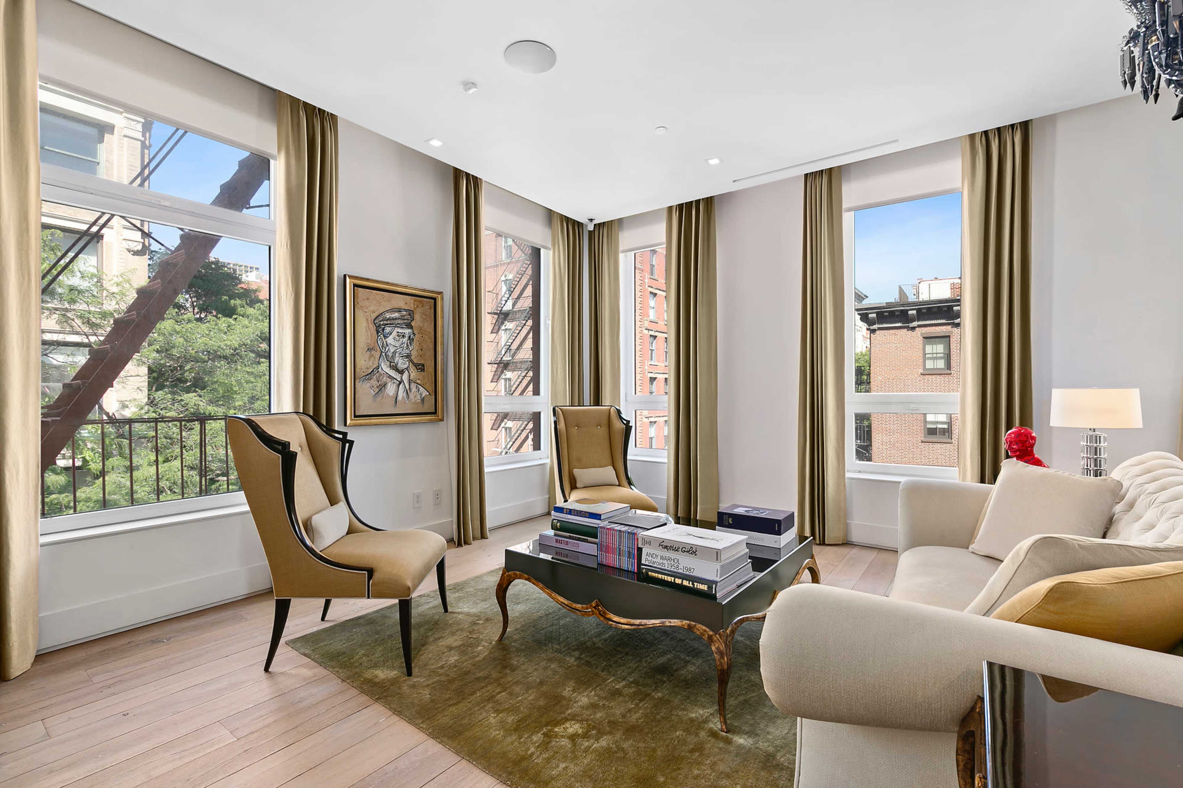 A bright living room with large windows, two armchairs, a sofa, and a coffee table displaying books.