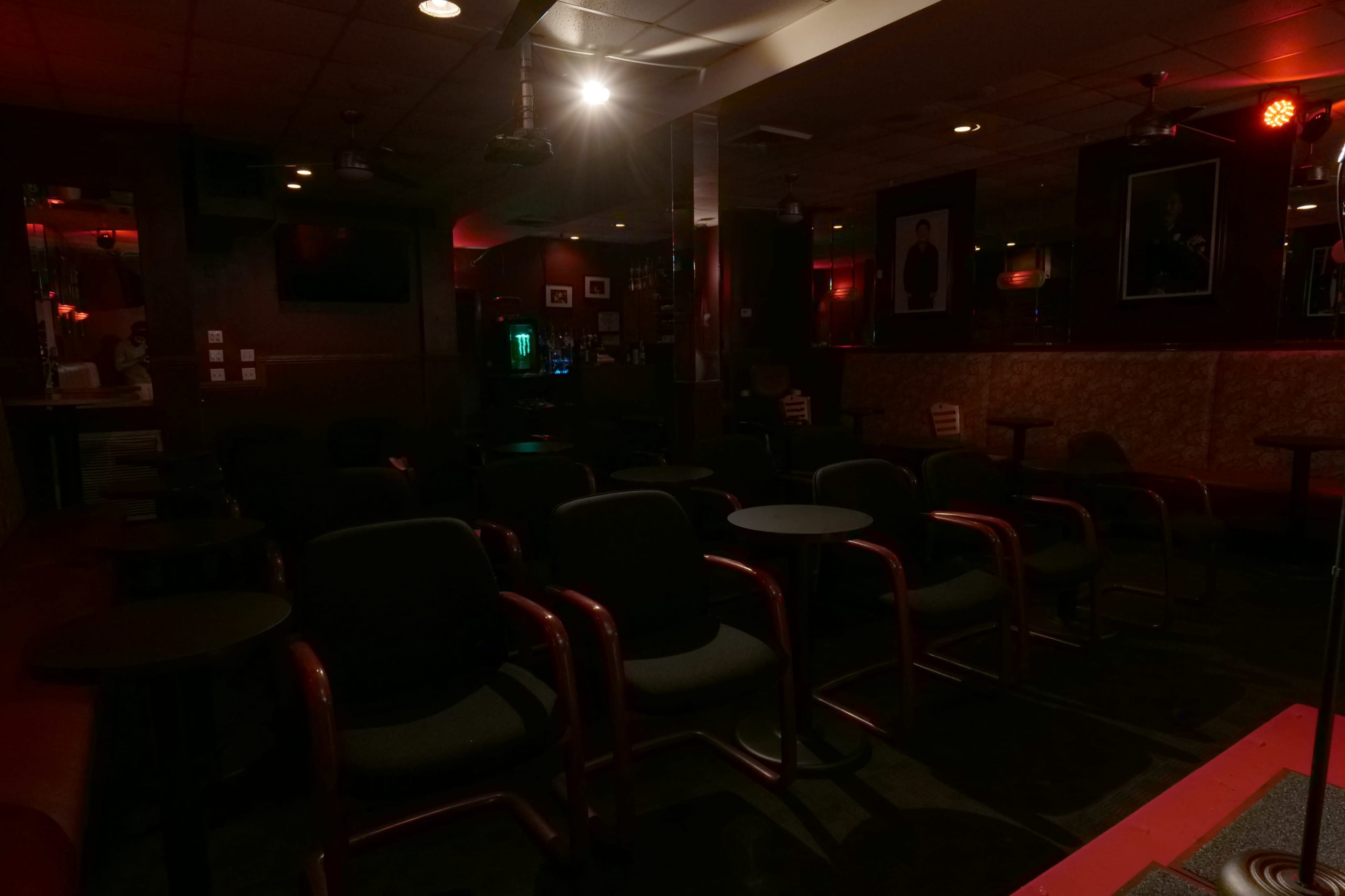 A dimly lit lounge features empty chairs and tables arranged in rows against red-tinted walls.