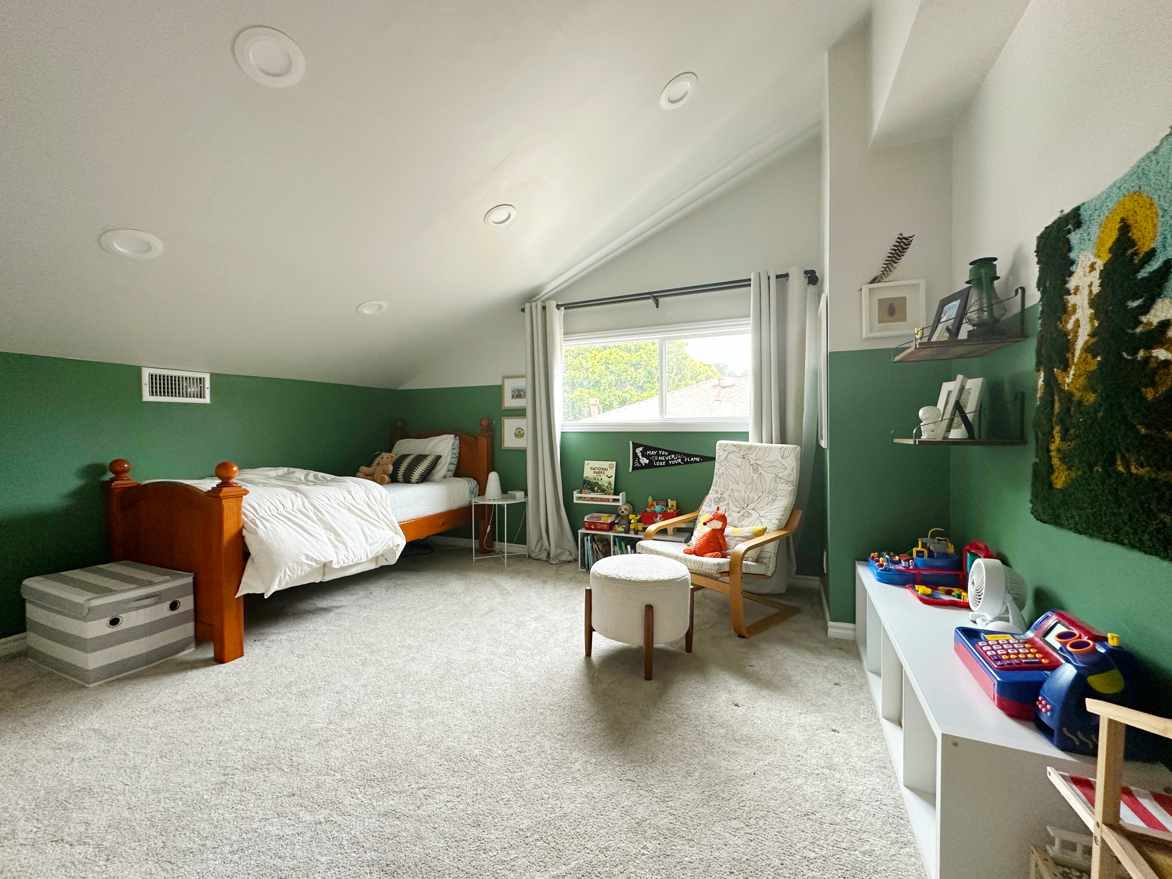 The image shows a cozy bedroom with a wooden bed, a rocking chair, and various toys arranged on shelves against green walls.