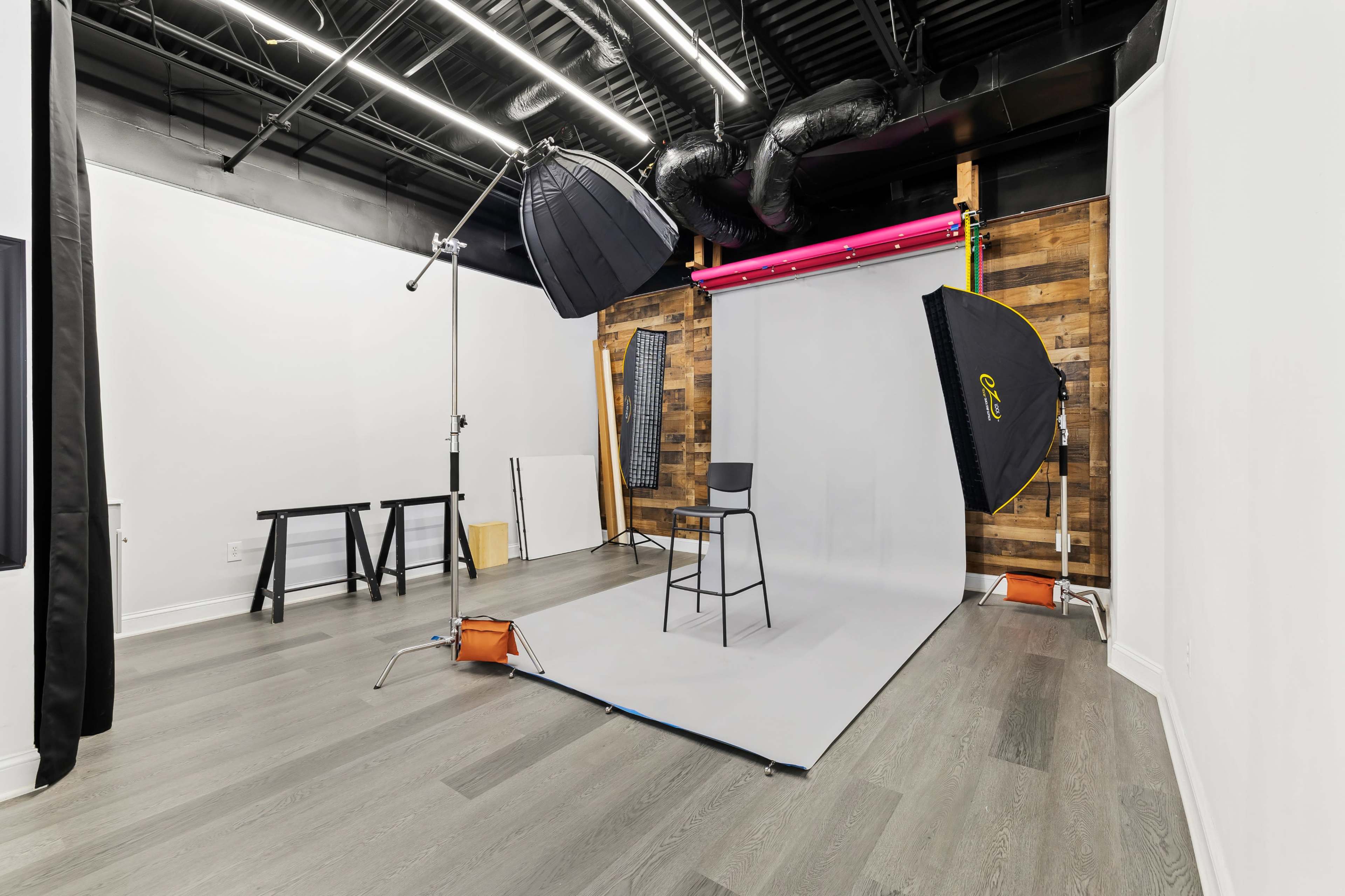 A photography studio with a gray backdrop, a black chair, and various lighting equipment set up in a modern interior space.