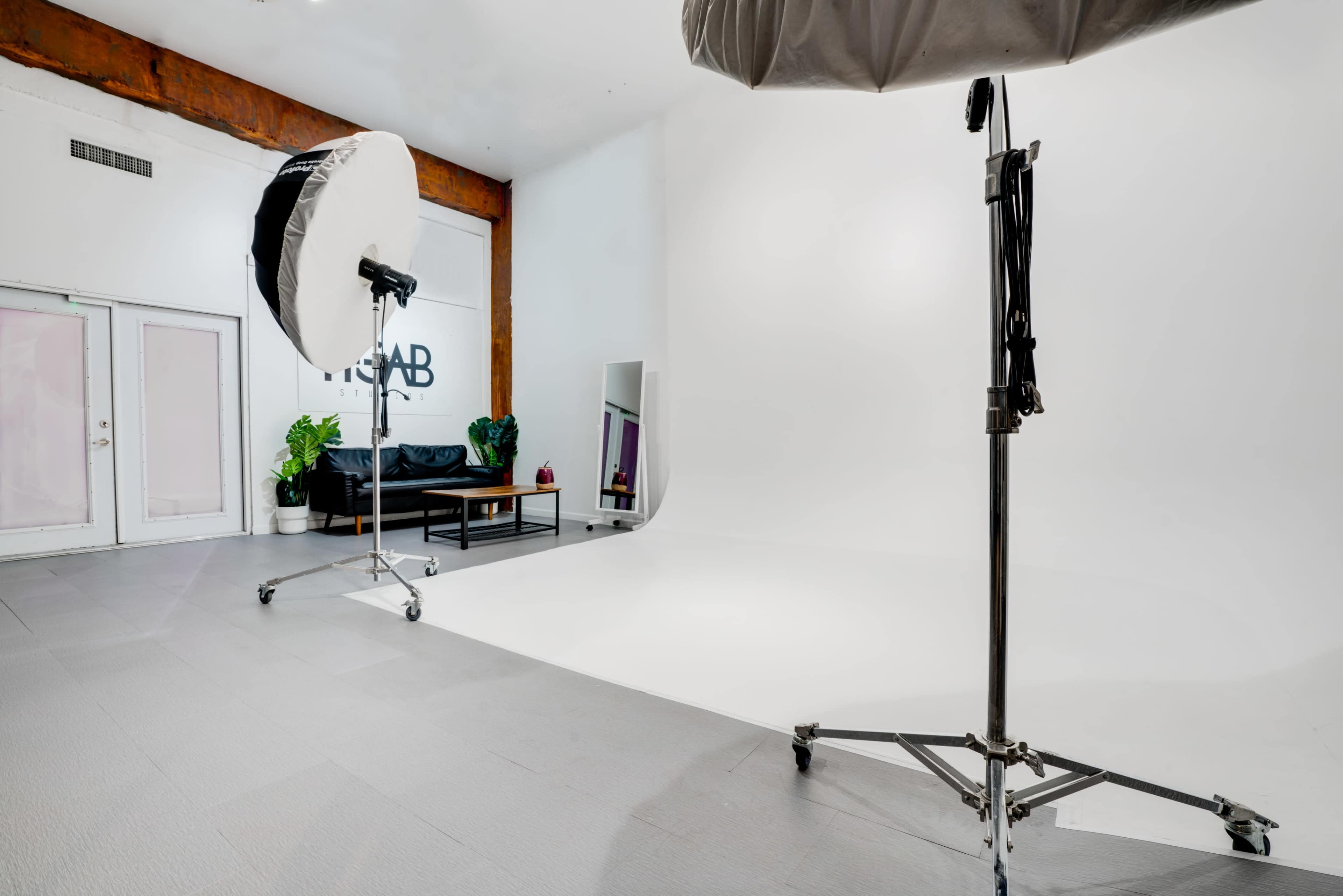 A photography studio with large softboxes, a white backdrop, and a black couch against a wall with the word "STAB" visible.