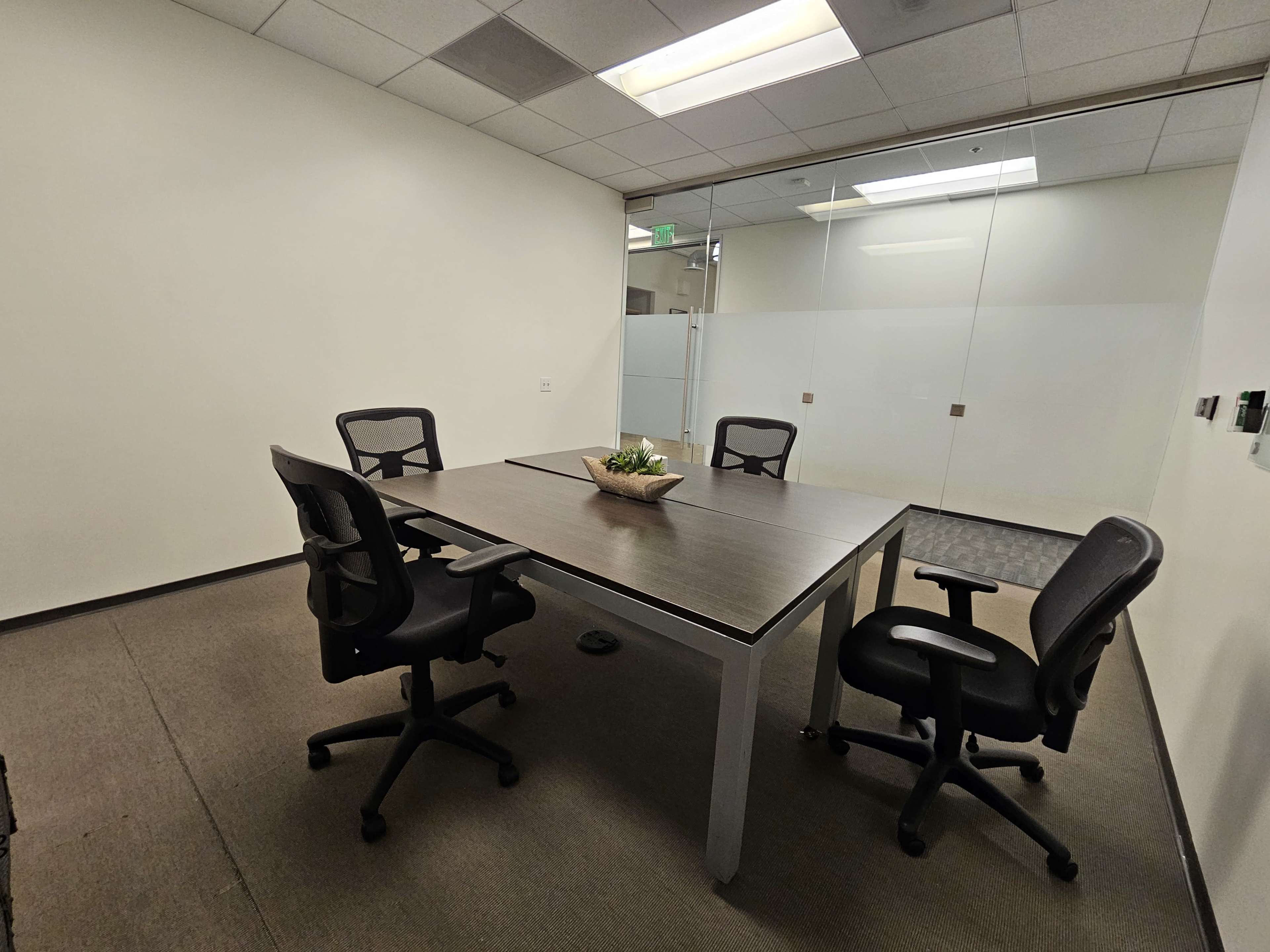 The image shows a conference room with a rectangular table and four rolling office chairs arranged around it.