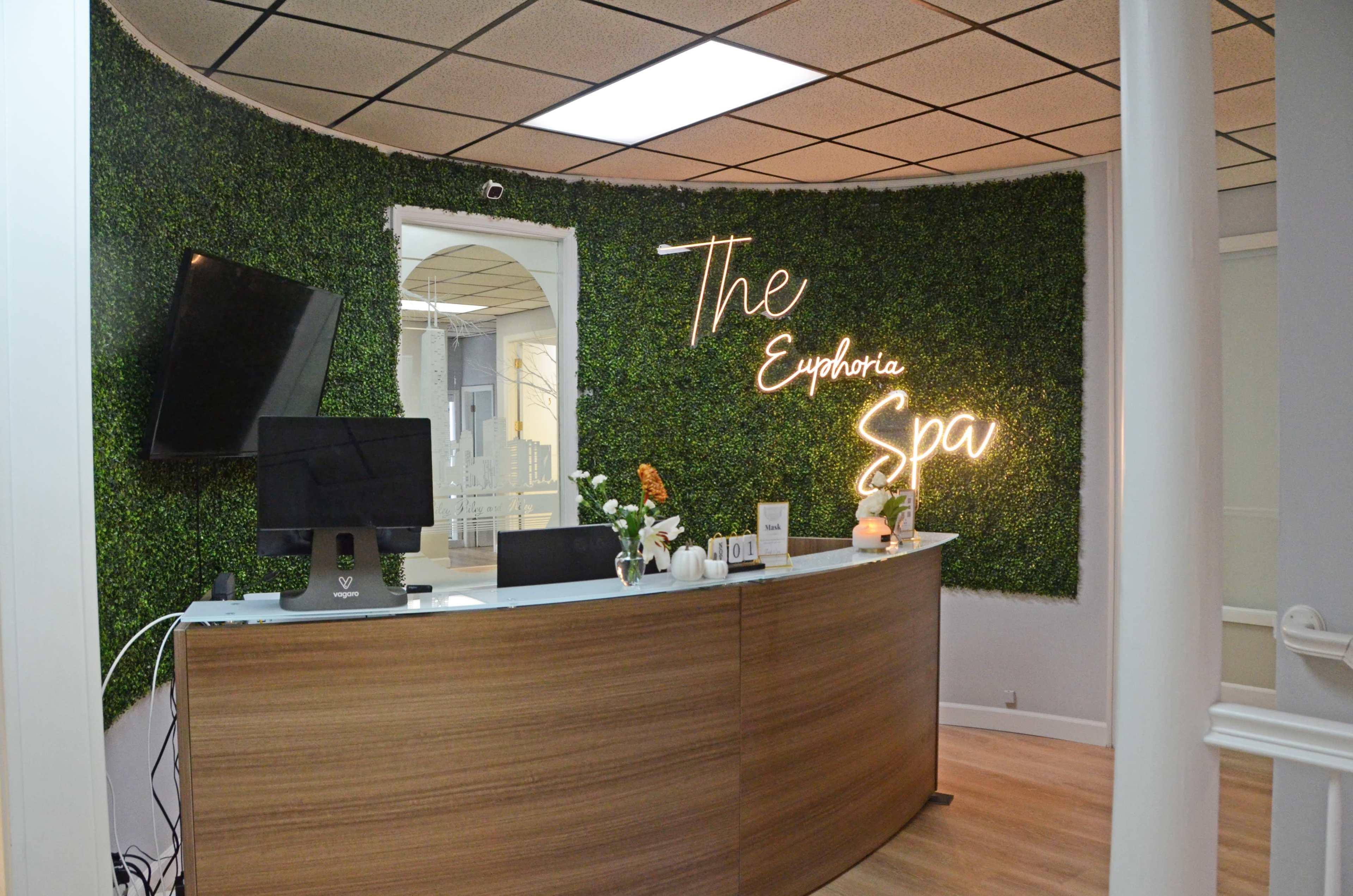 The reception area of Euphoria Spa features a curved wooden desk against a green wall with a neon sign.