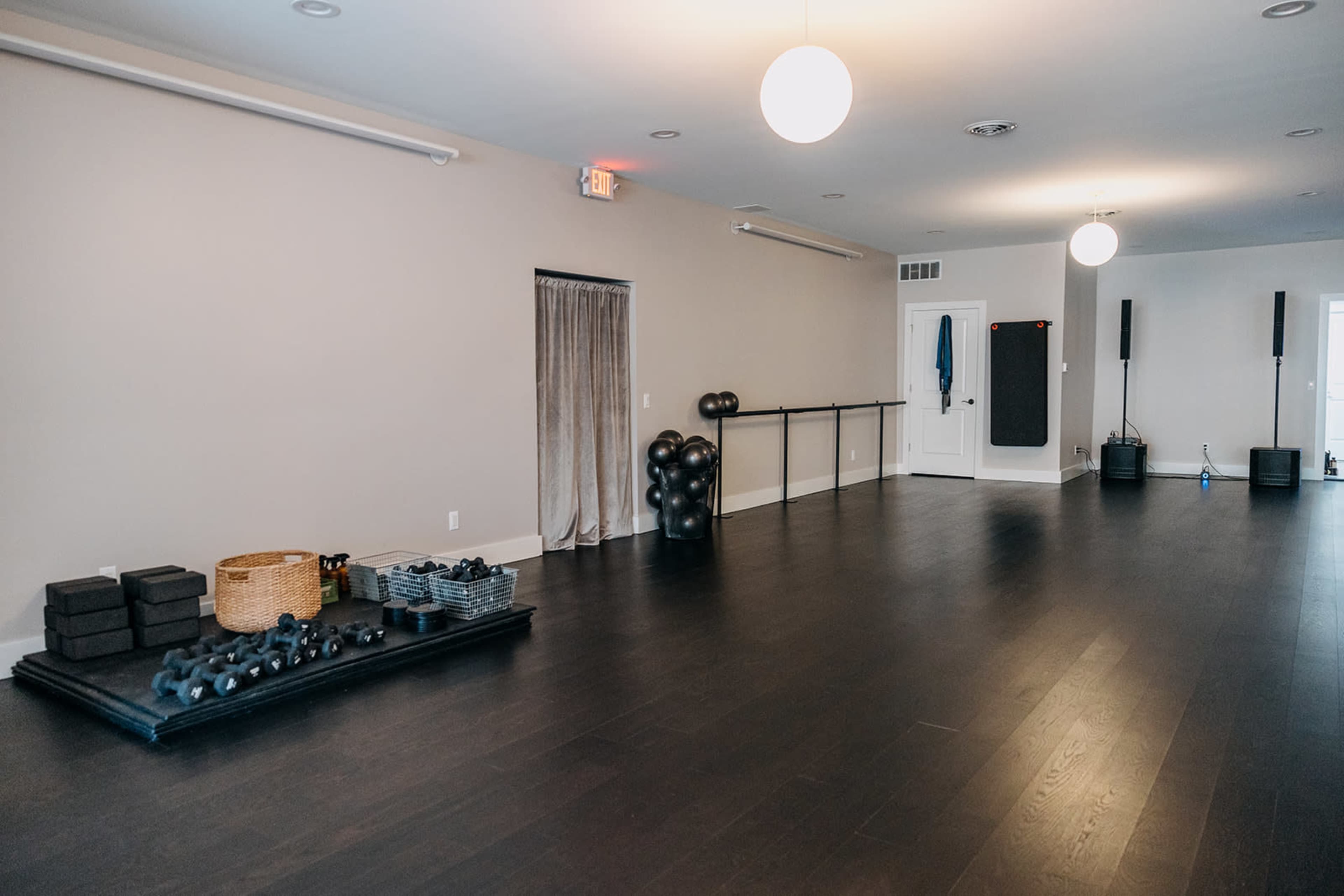 A spacious, empty room with dark wooden floors, a barre against one wall, and various fitness equipment neatly arranged on the floor.