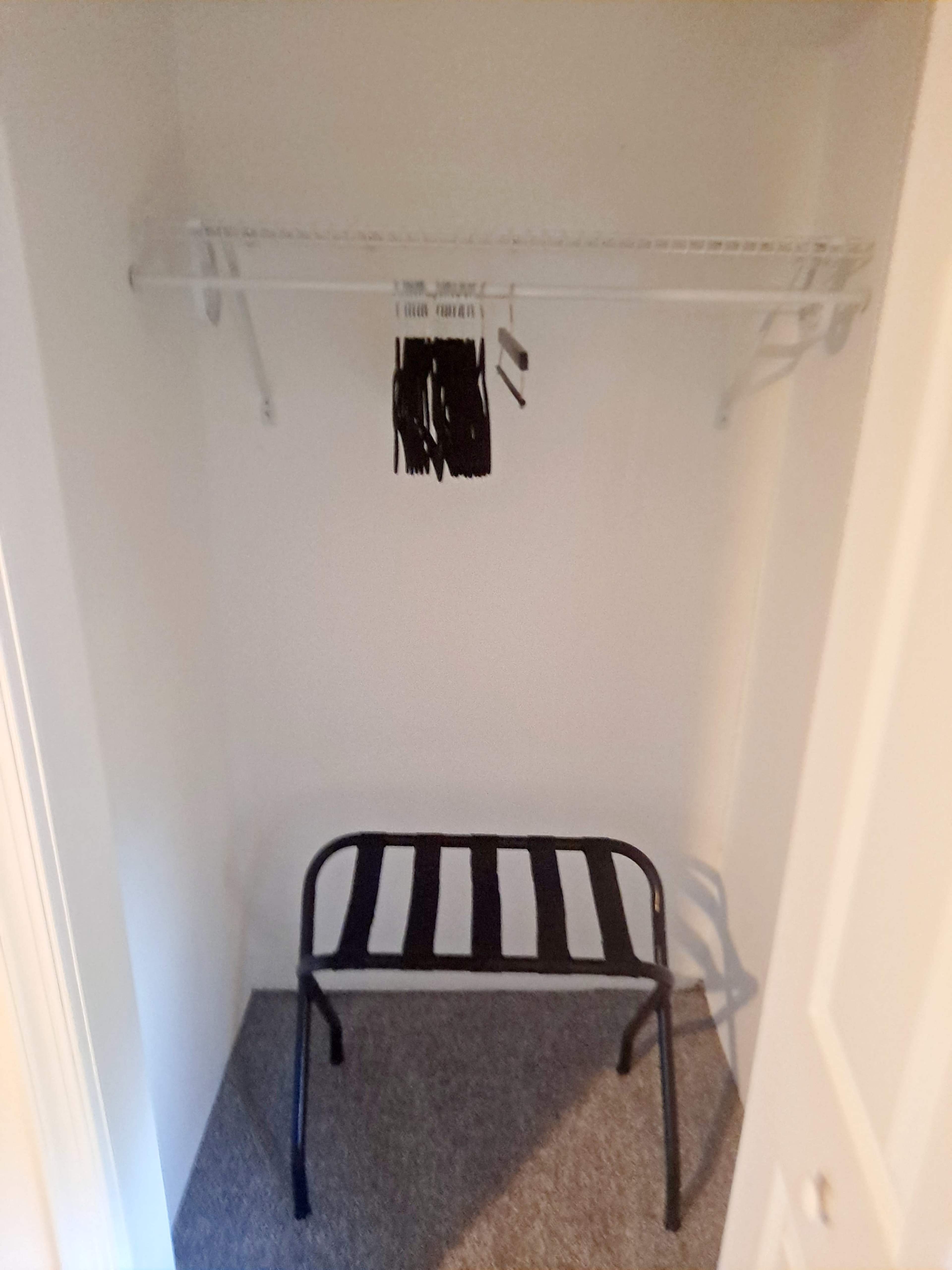 A small closet with a black folding chair, a wire shelf above it, and a few hanging items.