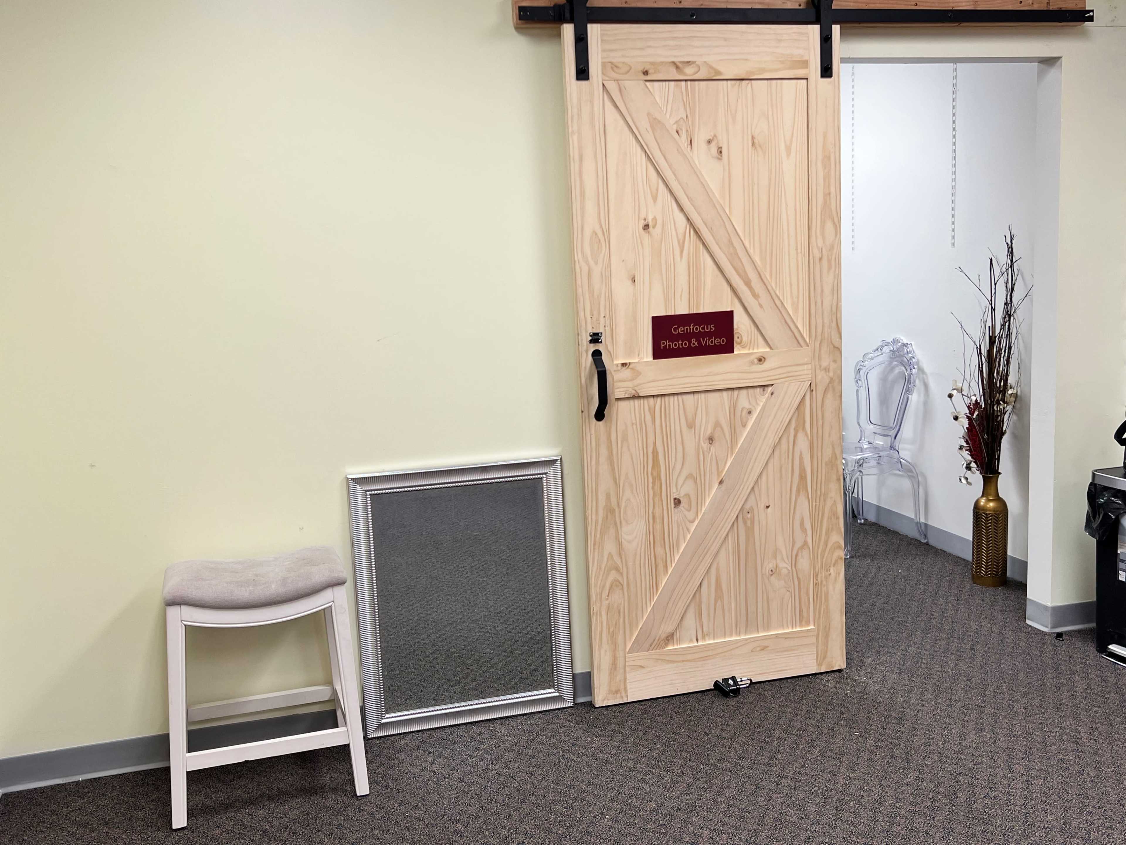 A wooden sliding door is partially open to reveal a room, with a mirror leaning against a wall and a stool placed nearby.