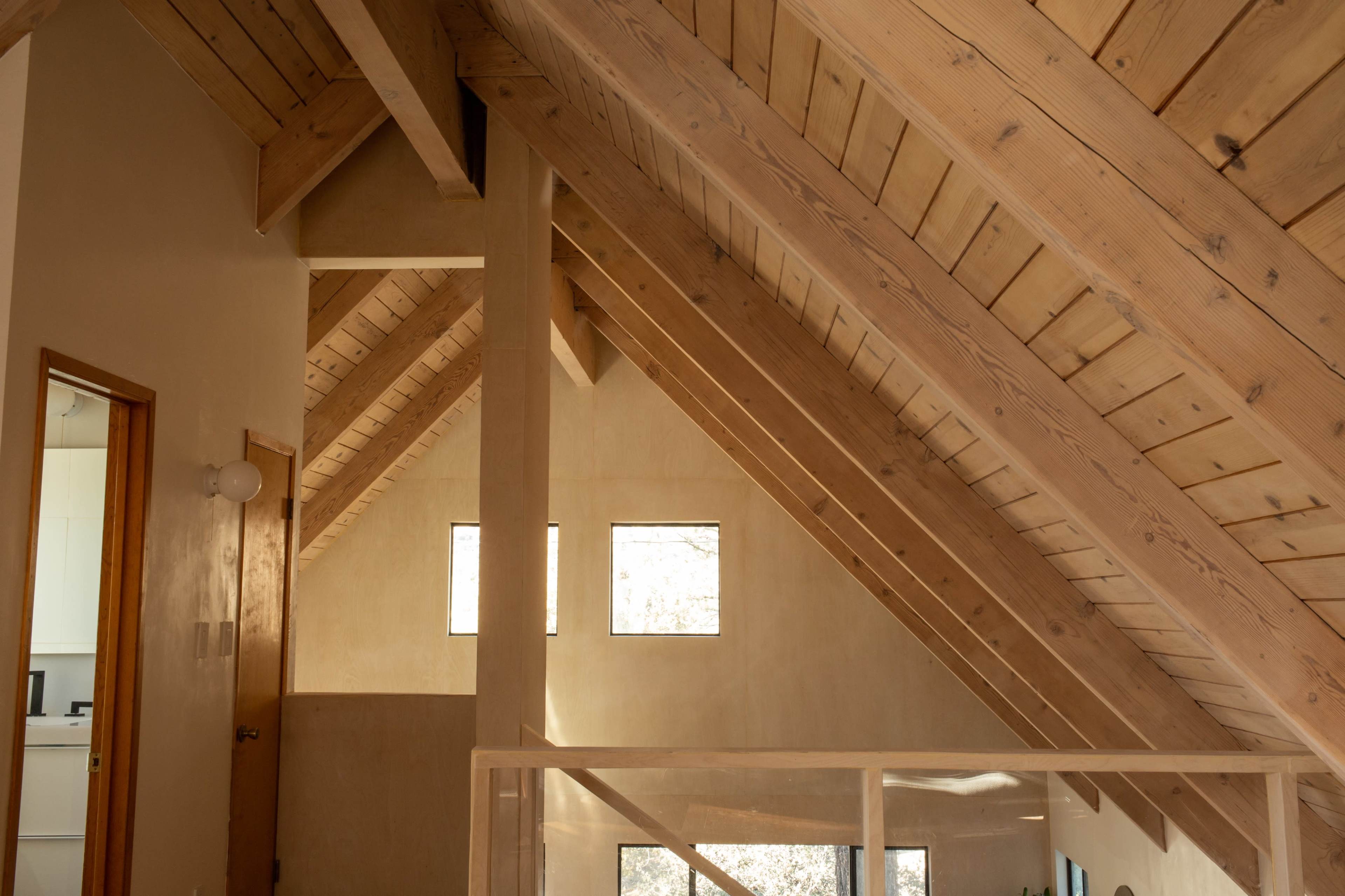 An interior space with exposed wooden beams and a sloped ceiling, featuring windows that allow natural light to enter.