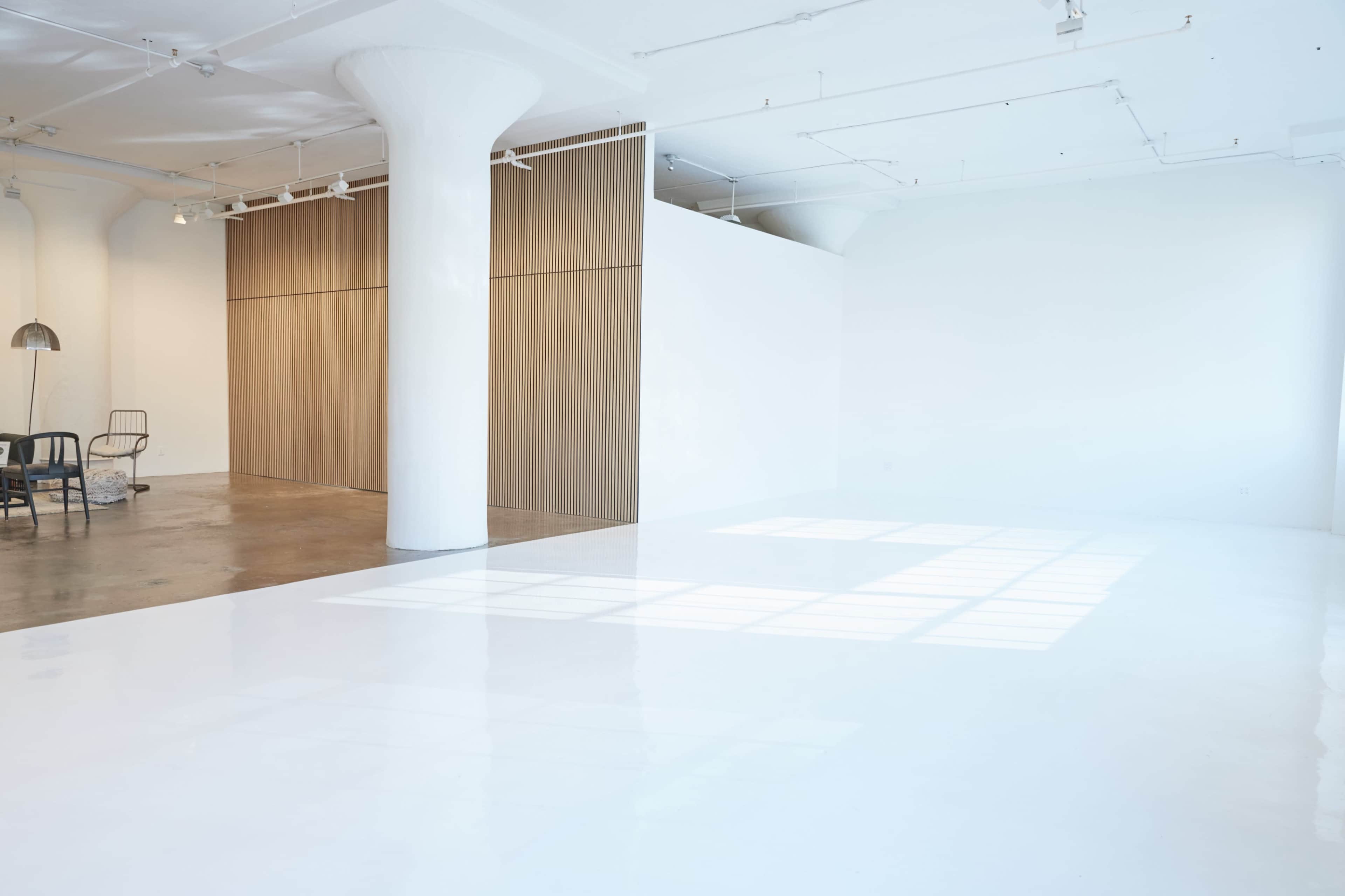 A spacious, brightly lit interior with a polished white floor, large windows, and wooden paneling on one wall.