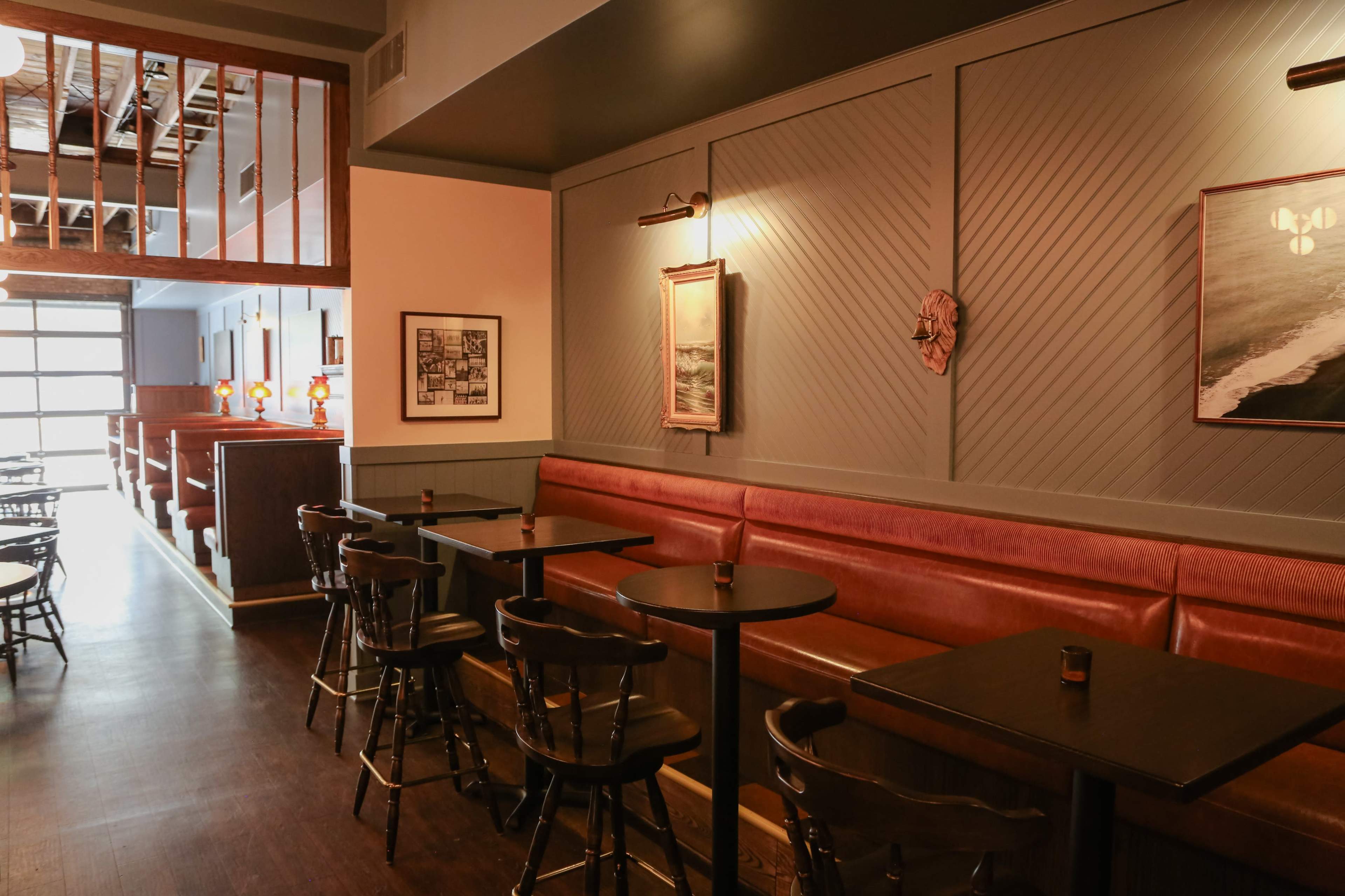 The image shows the interior of a restaurant featuring wooden tables, leather seating along the wall, and framed artwork on the walls.
