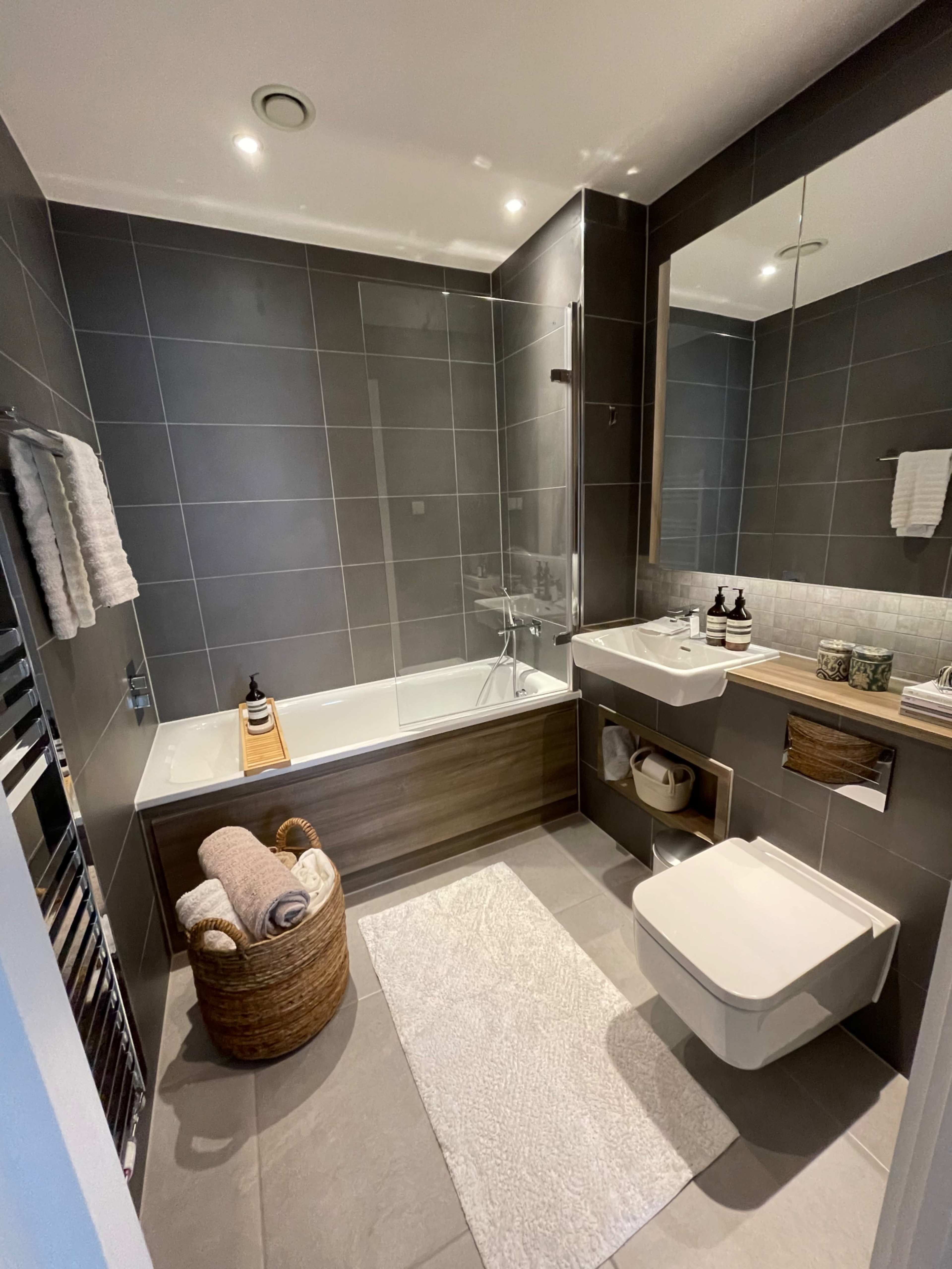 The image shows a modern bathroom featuring a bathtub with a shower, a wooden vanity with a sink, and a towel rack.