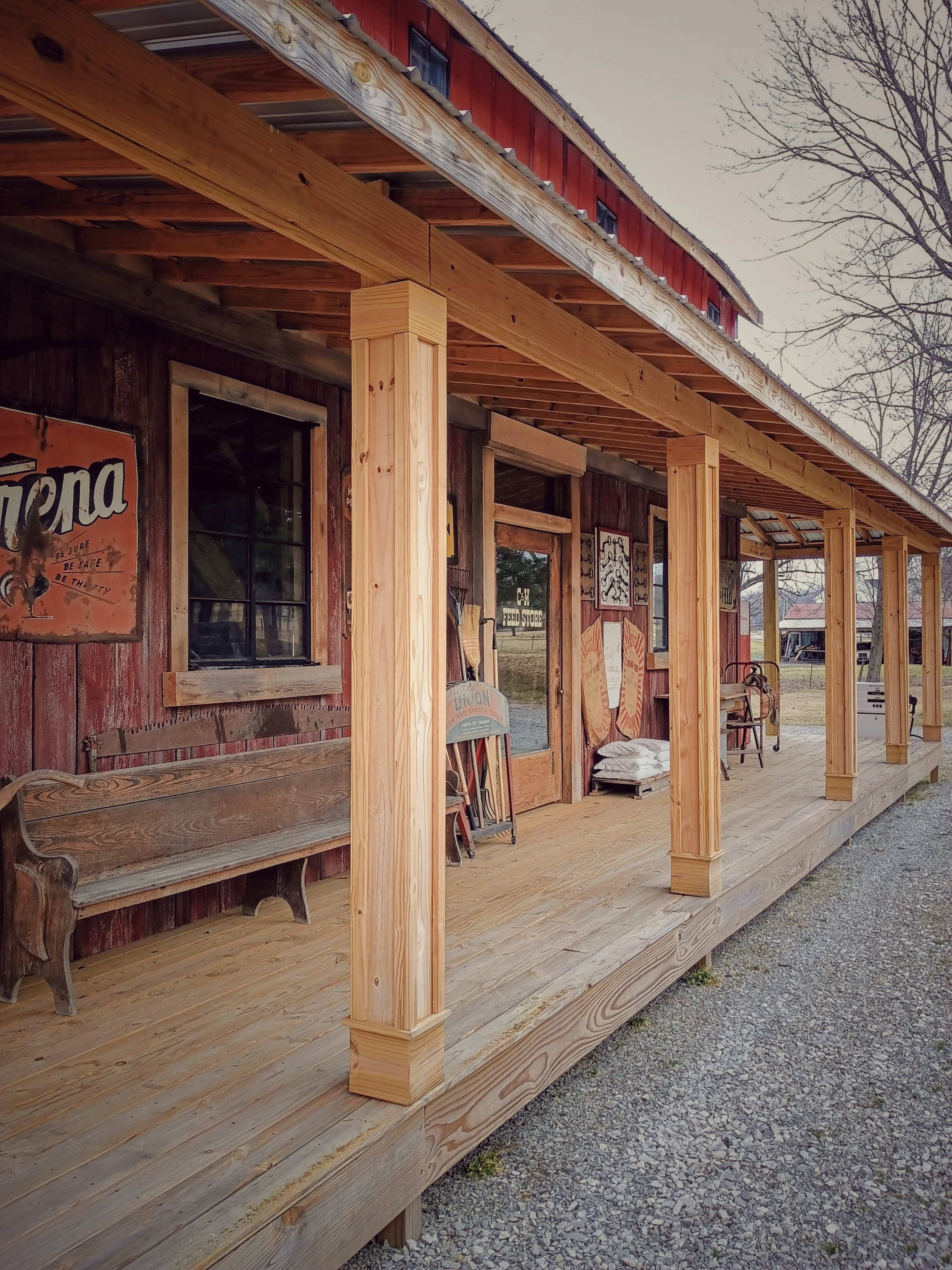 The image shows a rustic wooden porch with posts, leading up to a weathered red building.