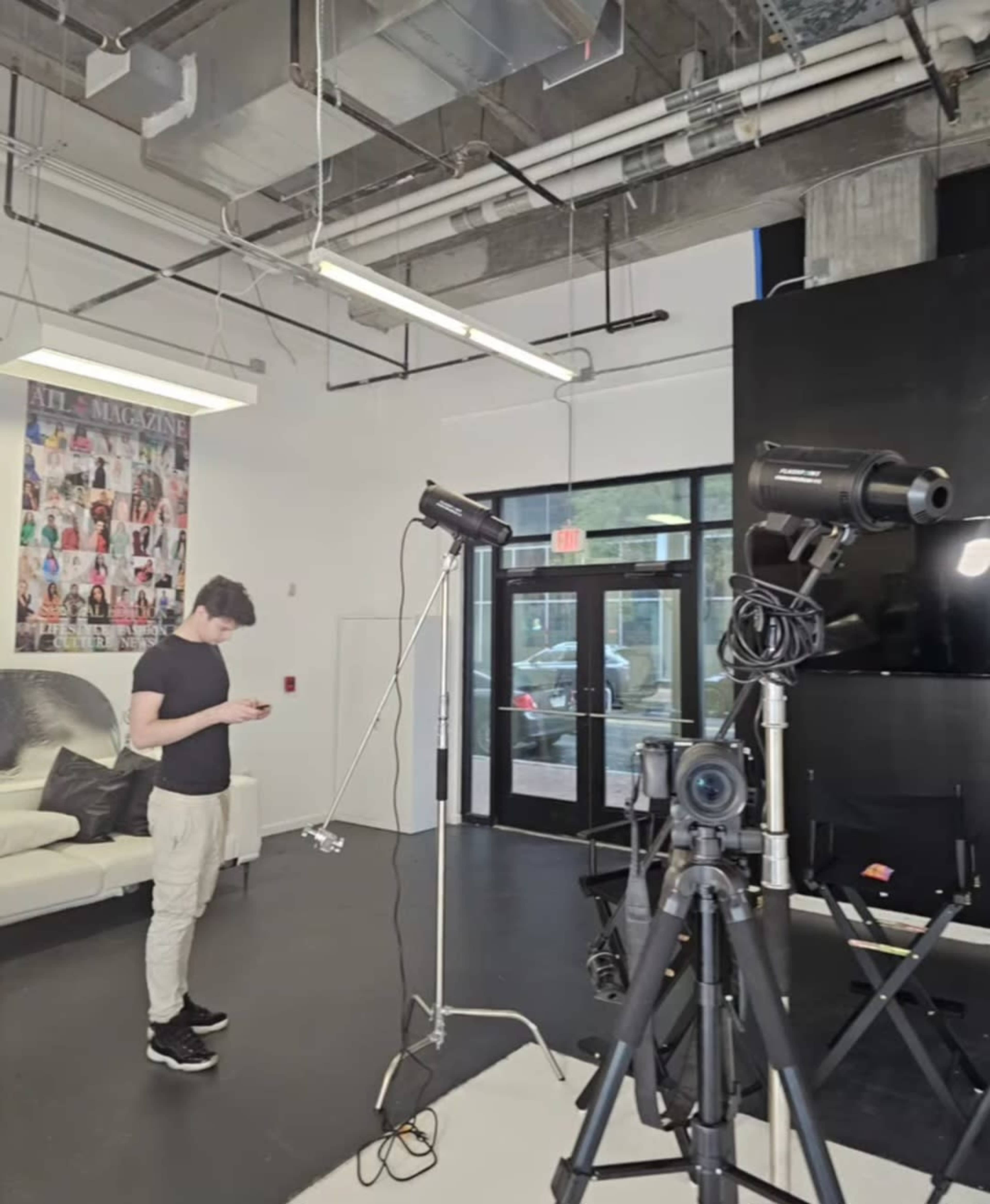 A person stands in a modern studio space, checking a device while photography equipment is set up nearby.