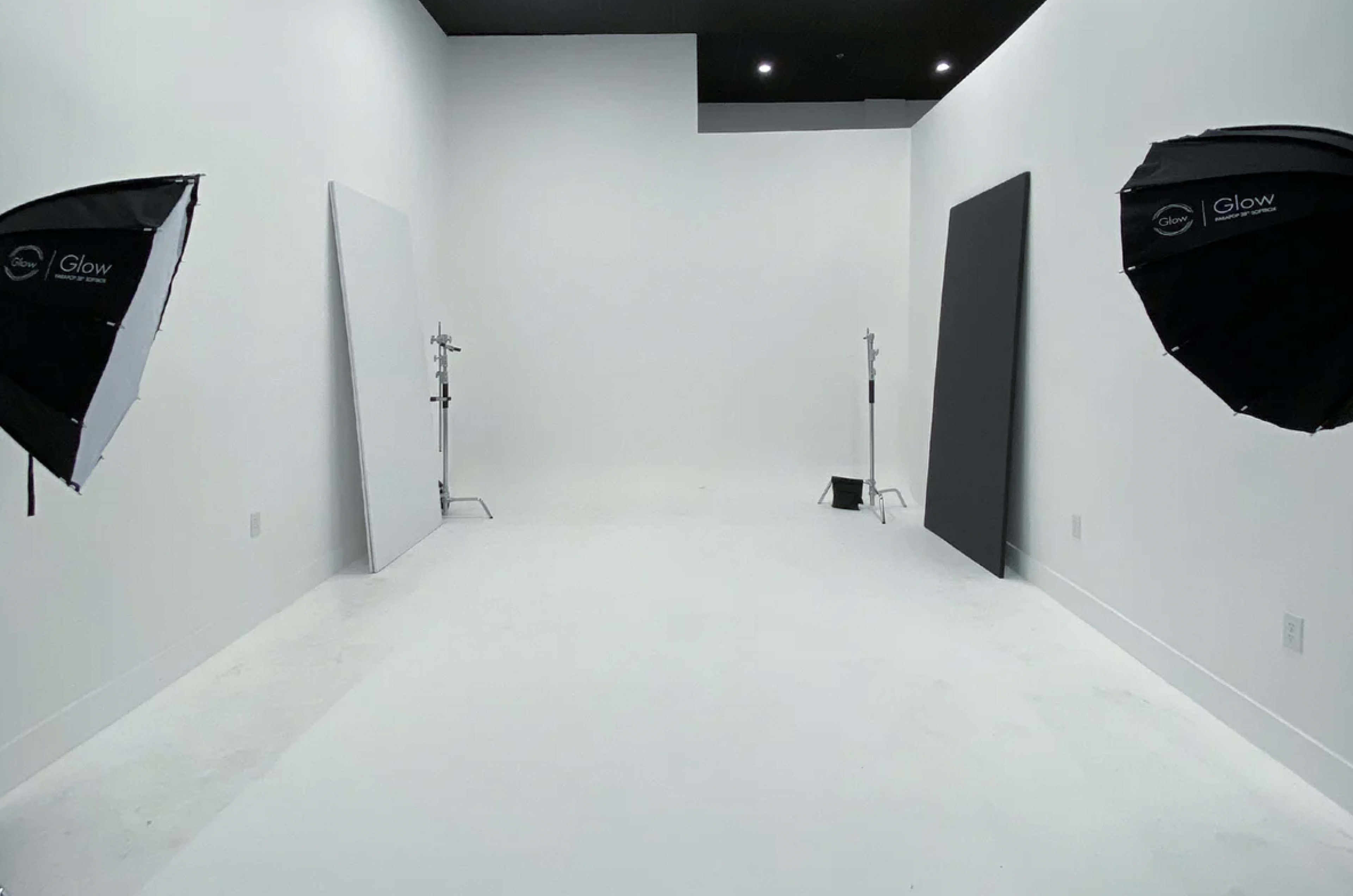 A spacious photography studio with white walls and two lighting setups on either side.
