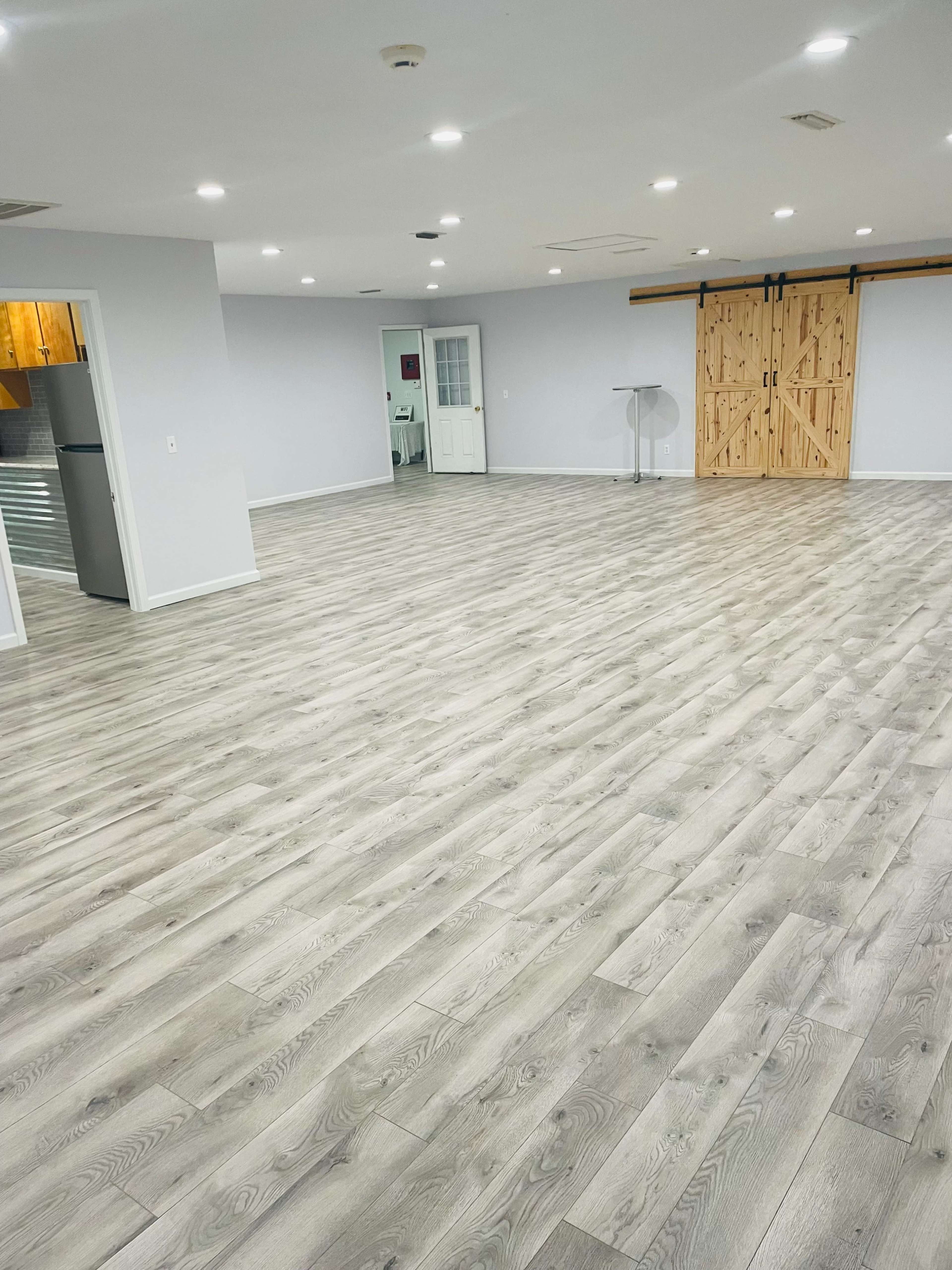 A spacious room with light-colored wooden flooring and a wooden sliding barn door in the background.